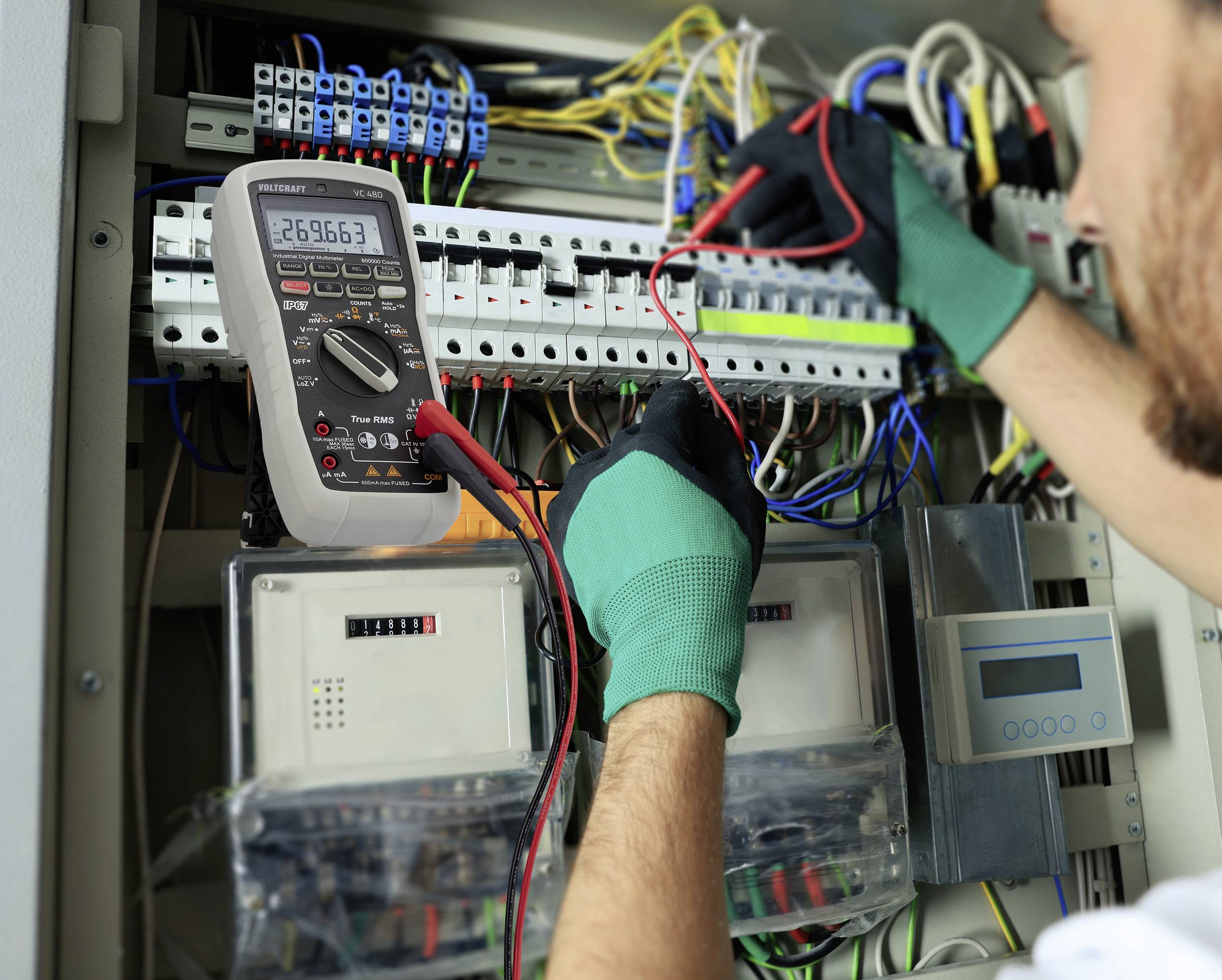 Un technicien teste les connexions électriques dans un armoire électrique à l'aide d'un multimètre qui affiche une valeur de 269,663.