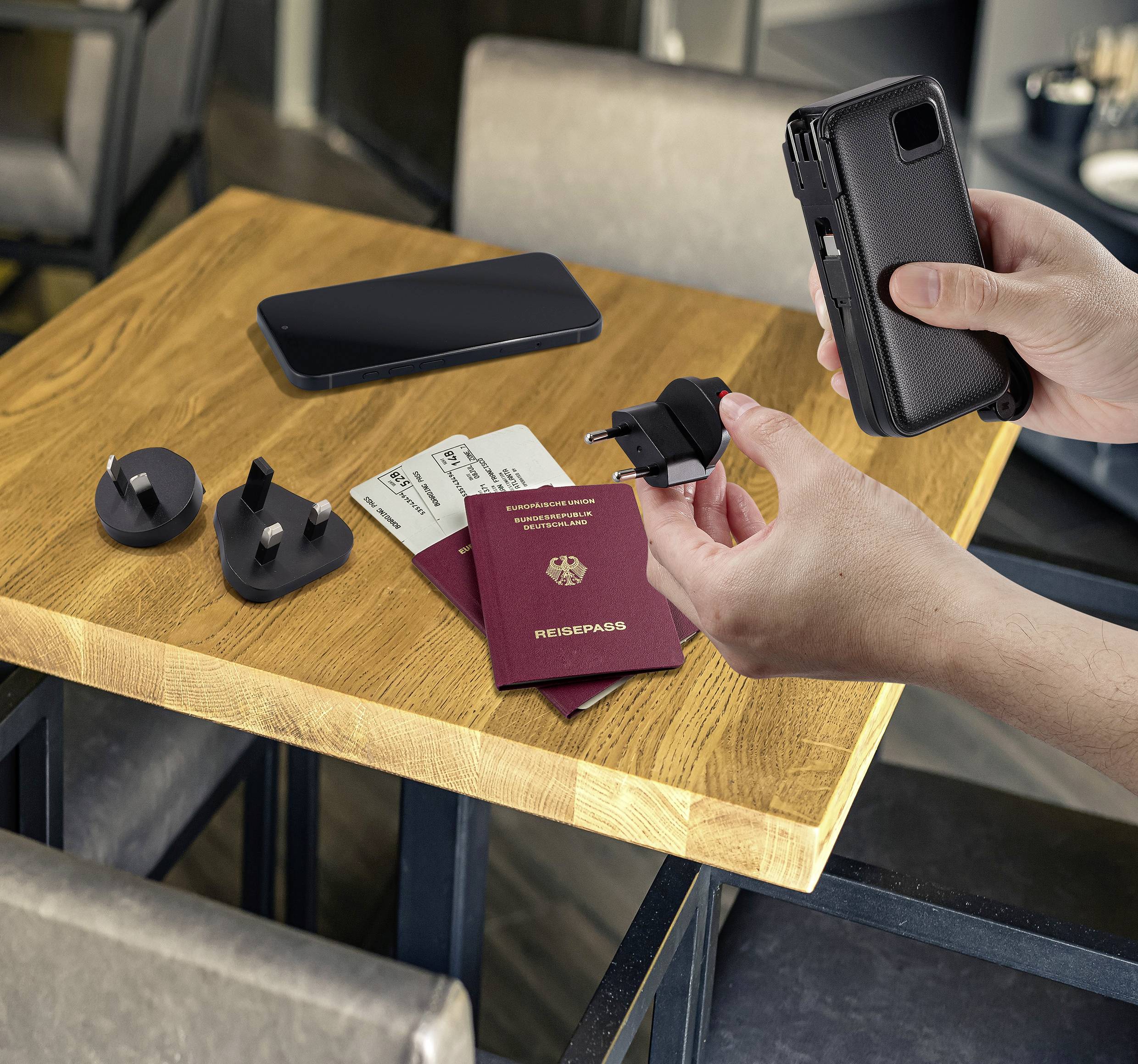 Une personne tient un adaptateur à côté d'un smartphone et de deux passeports sur une table. Des billets d'avion sont posés près des passeports.