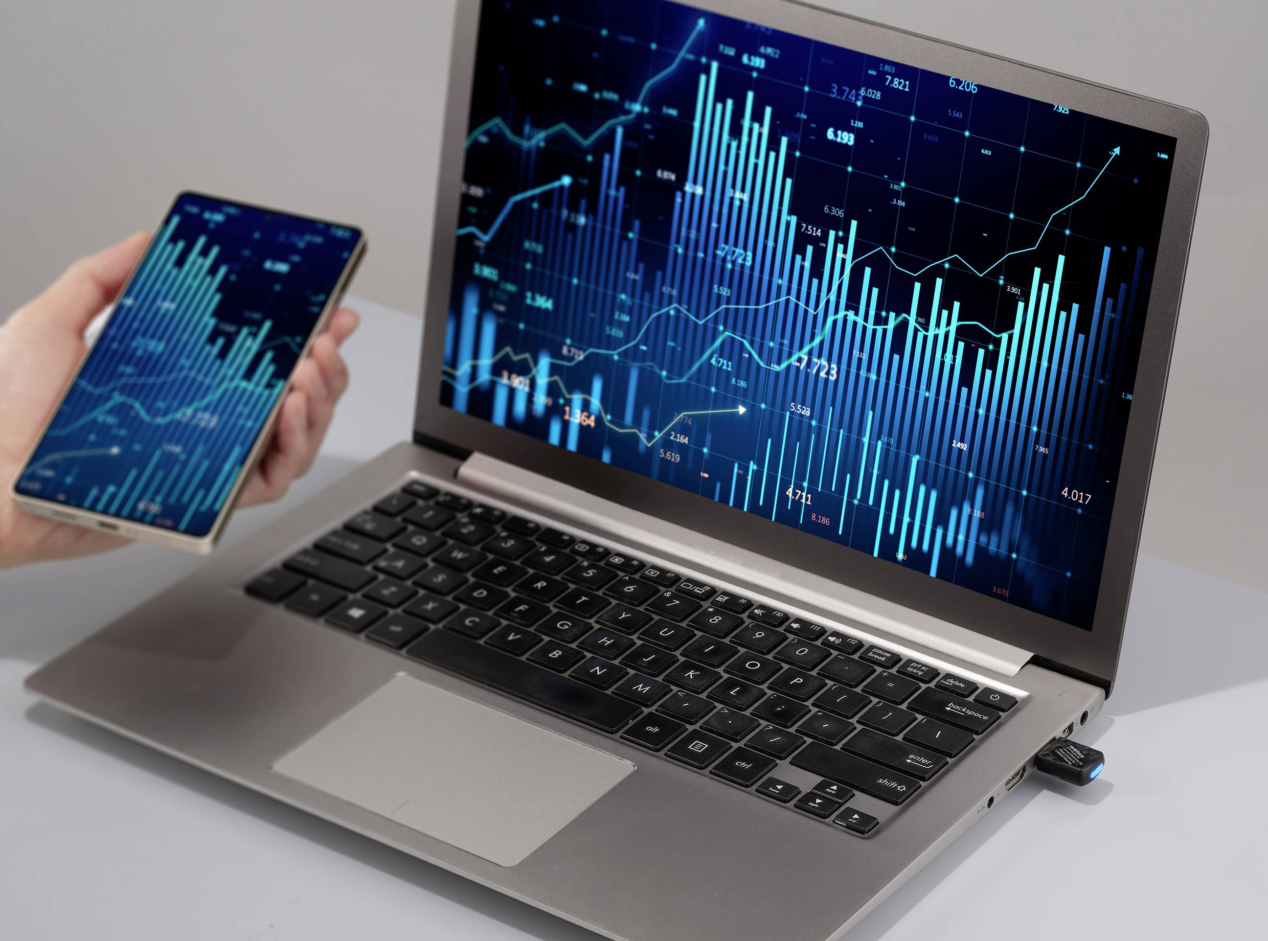 Un ordinateur portable et un smartphone affichent des diagrammes financiers complexes avec des barres et des lignes représentant des tendances et des données en temps réel.