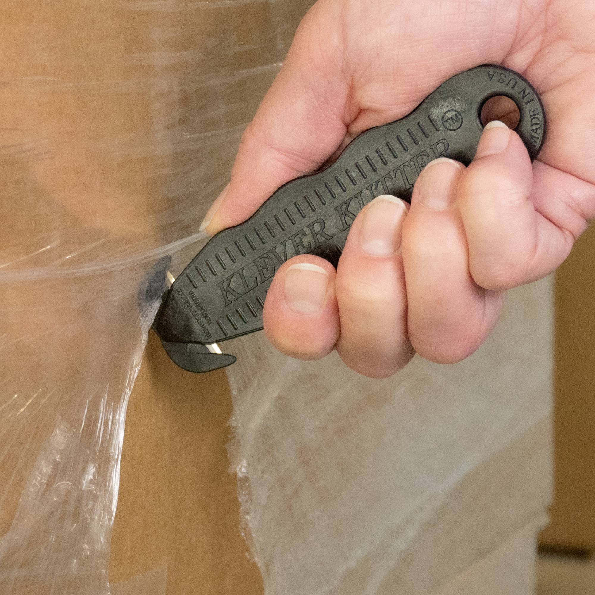 Une main tient un couteau de sécurité et coupe du carton. La lame rétractable est cachée, réduisant ainsi le risque de blessure.