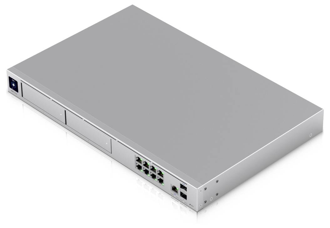 Commutateur réseau argenté avec plusieurs ports Ethernet et deux emplacements vides à l'avant, posé sur une surface blanche.