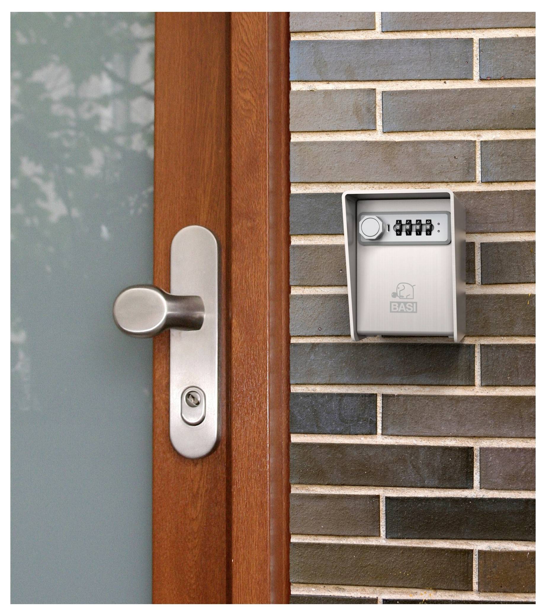 A keypad lockbox is mounted on a brick wall next to a wooden door with a metallic handle, likely for secure key storage.