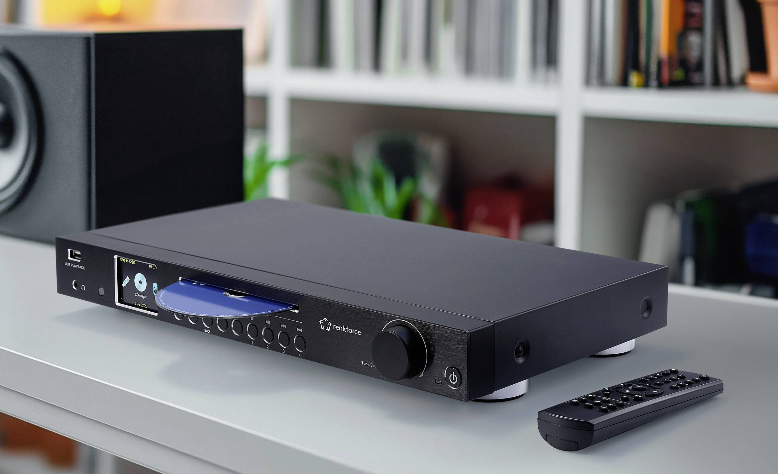 Un lecteur CD audio élégant est posé sur une table avec une télécommande à proximité. Des livres sont visibles sur une étagère blanche en arrière-plan.