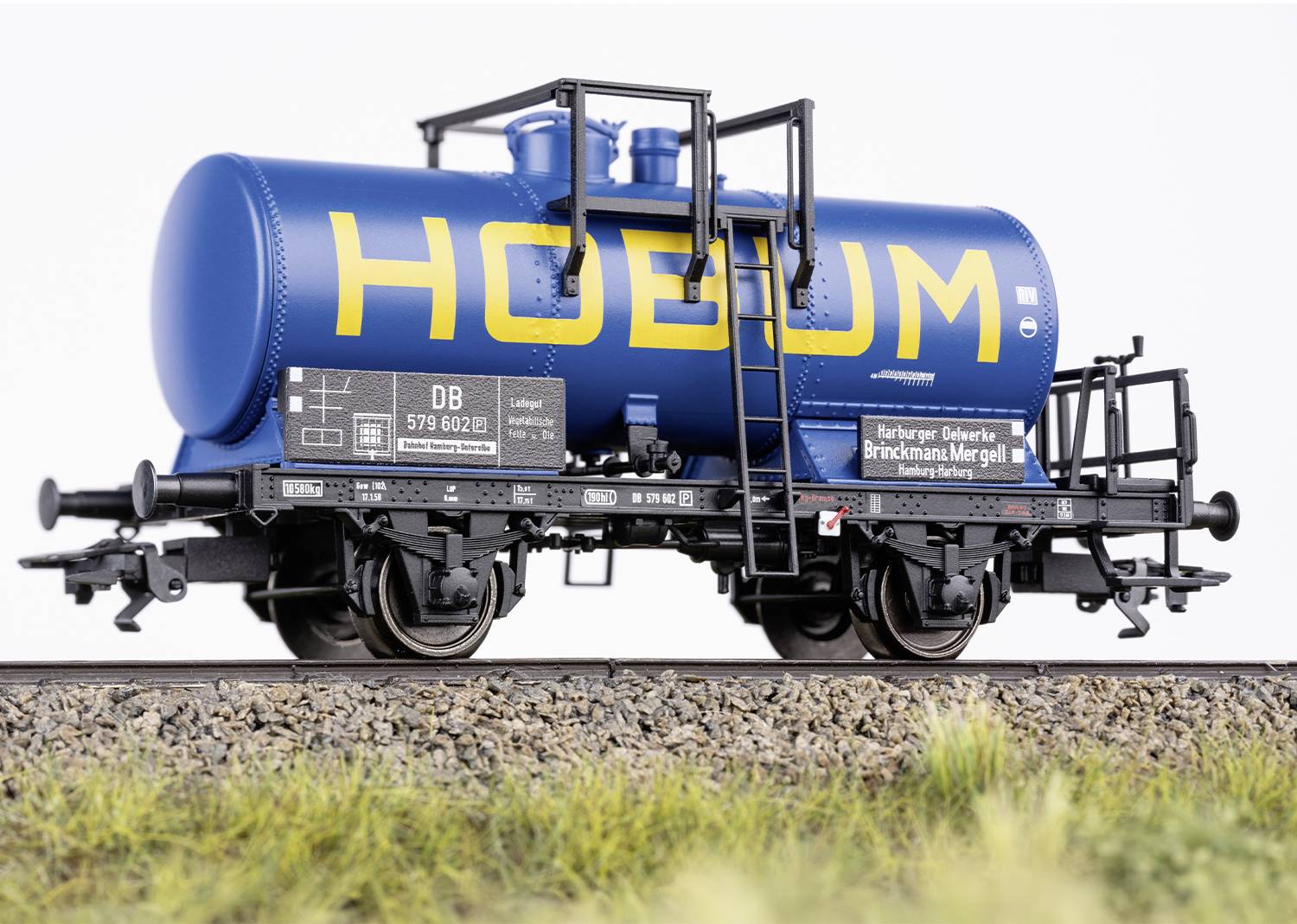 Un wagon-citerne de marchandises bleu avec l'inscription jaune 'HOBUM' est stationné sur des rails. Des inscriptions détaillées et des échelles sont visibles.