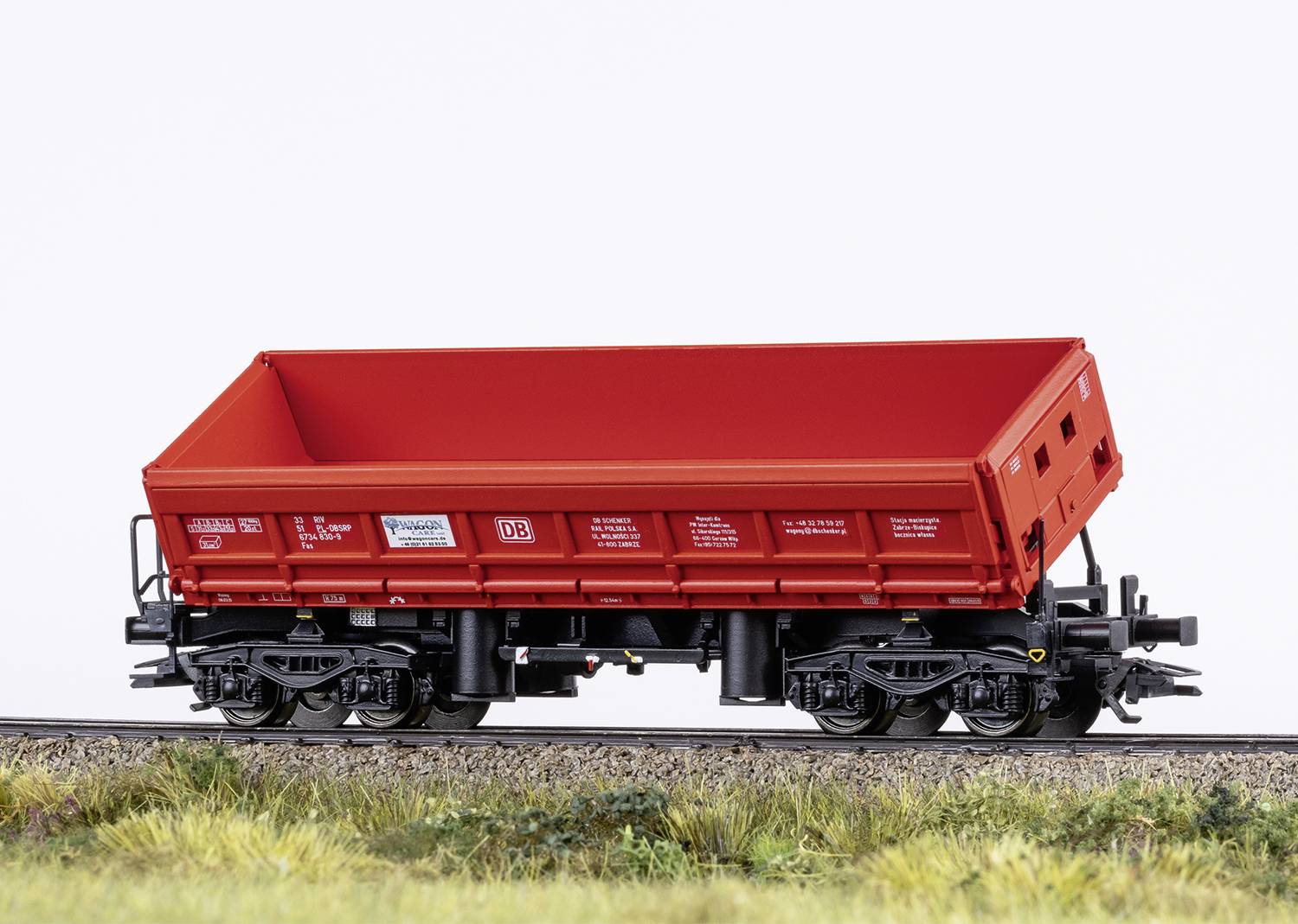 Un wagon de marchandises rouge sur des rails dans un paysage miniature. Le wagon est conçu avec de nombreux détails et présenté de manière réaliste.
