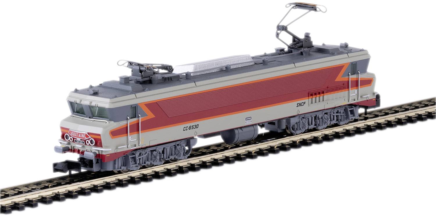 Un train miniature peint en gris et rouge sur un tronçon de voie ferrée. Le train présente des caténaires détaillées et des détails latéraux précis.