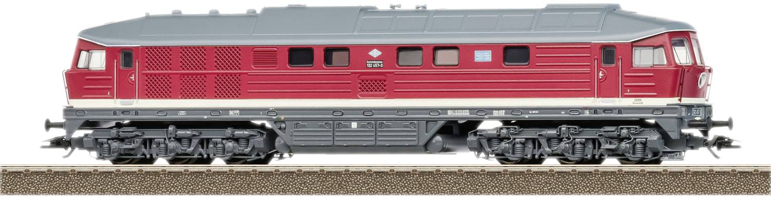 Une locomotive gris-rouge sur une voie ferrée, vue de côté, avec des grilles de ventilation distinctives et le soubassement des rails bien visible.