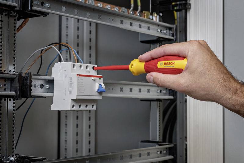 Une personne serre une vis avec un tournevis dans un coffret électrique. Des câbles sont connectés.