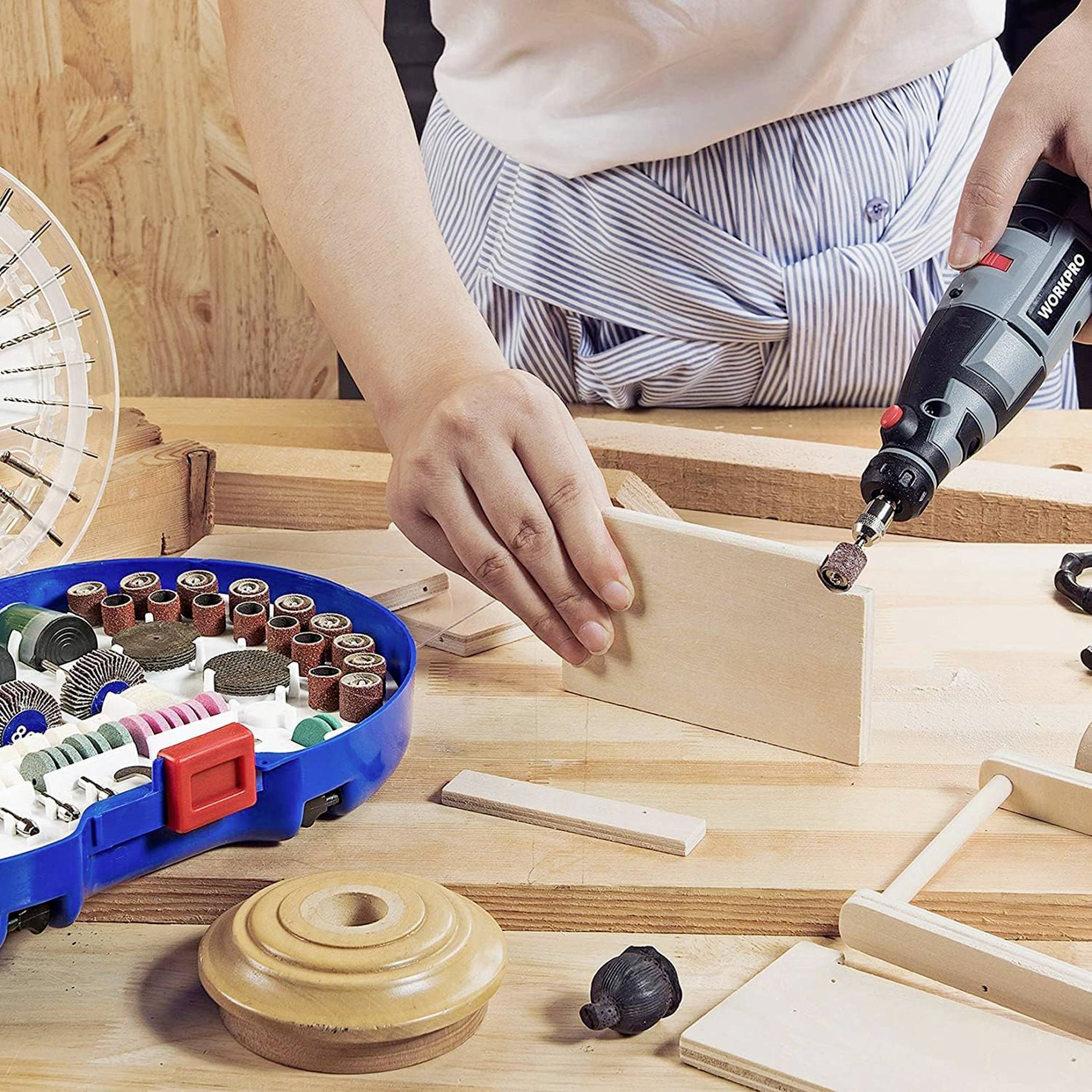 Une personne travaille un morceau de bois avec un outil électrique Dremel sur un établi. Des morceaux de bois et des outils sont disposés à proximité.
