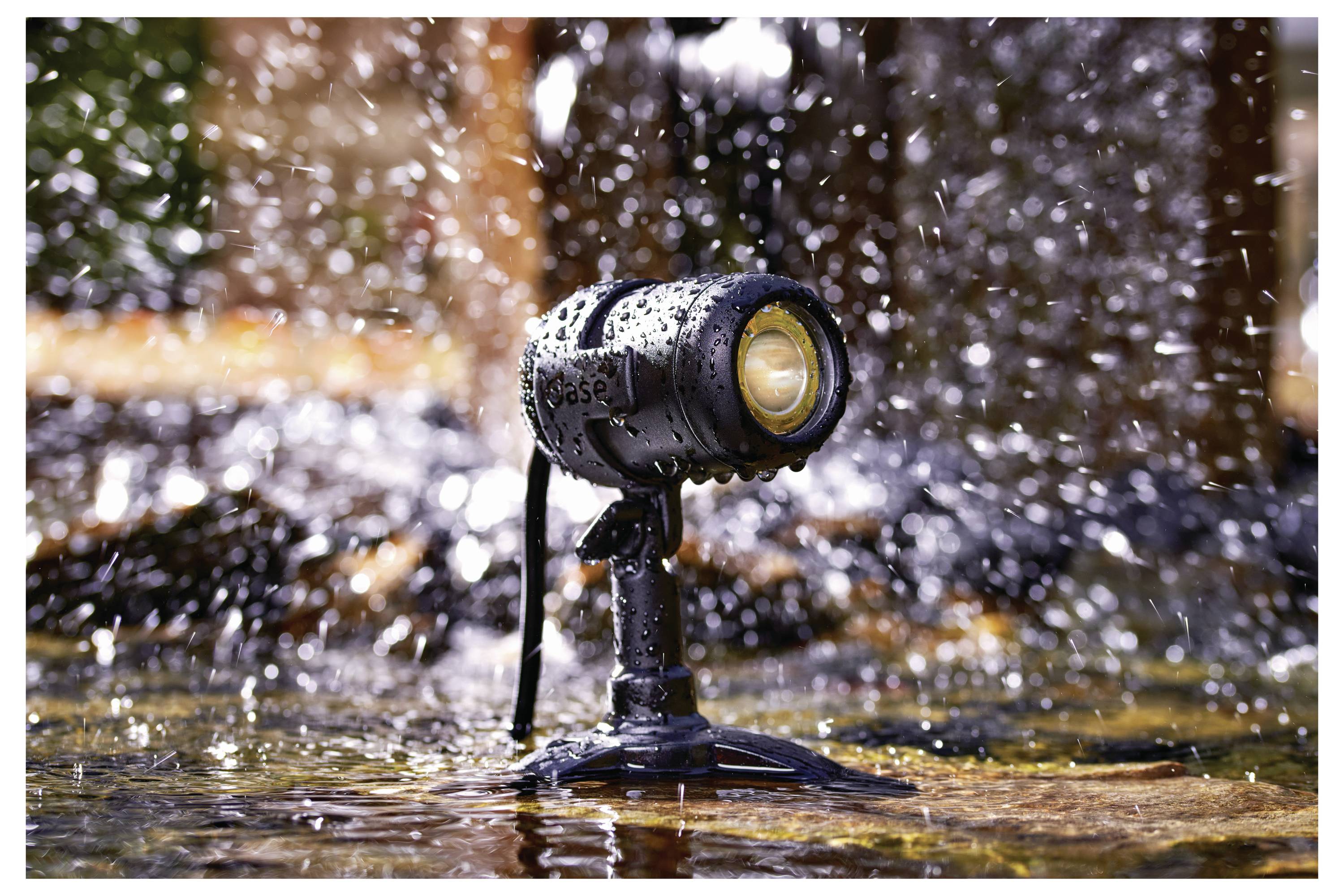 Un petit projecteur étanche couvert de gouttelettes d'eau est fixé sur une surface humide, avec des éclaboussures d'eau en arrière-plan.
