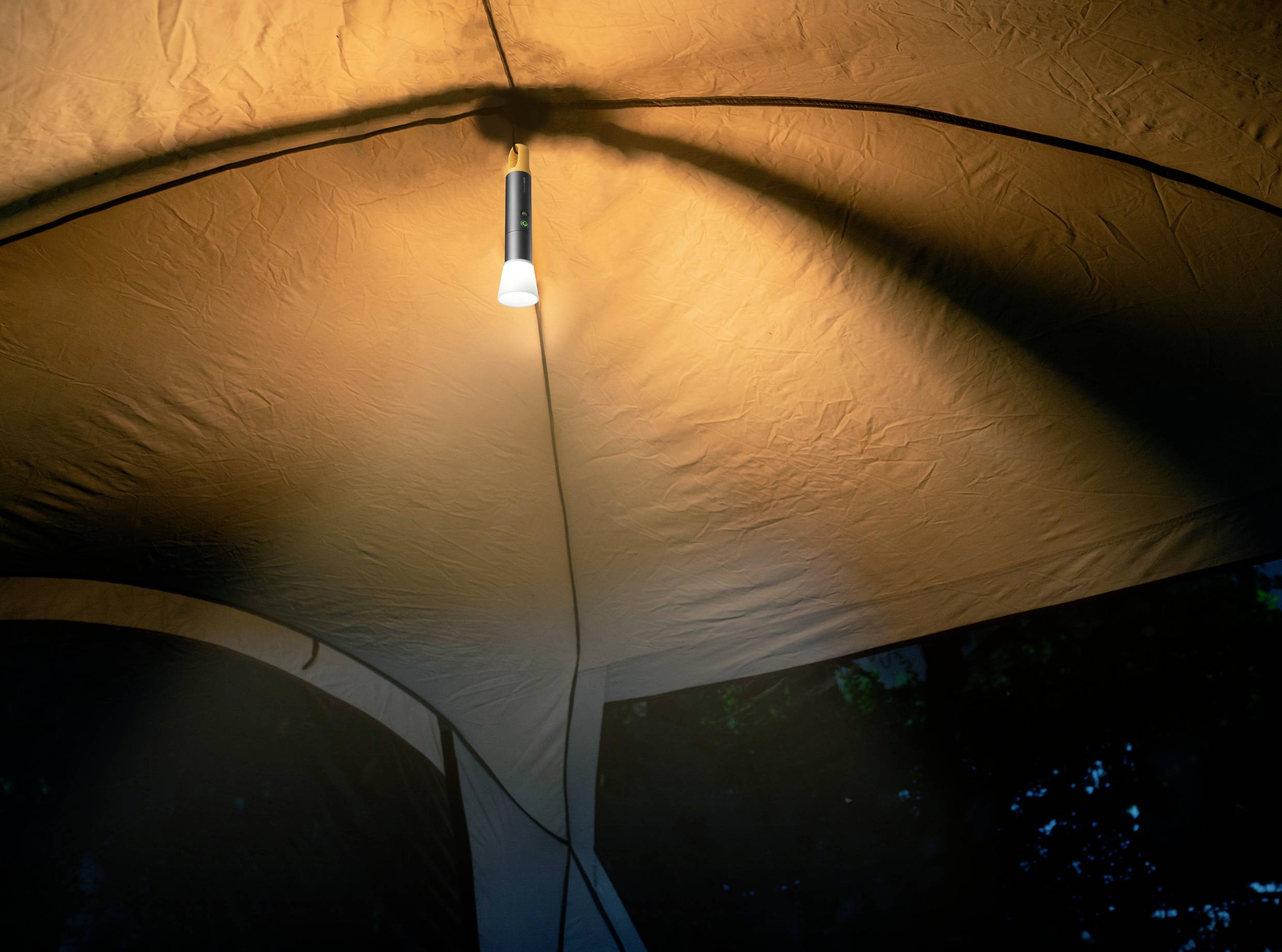 Vue intérieure d'une tente la nuit, éclairée par une ampoule suspendue qui crée une atmosphère chaleureuse.