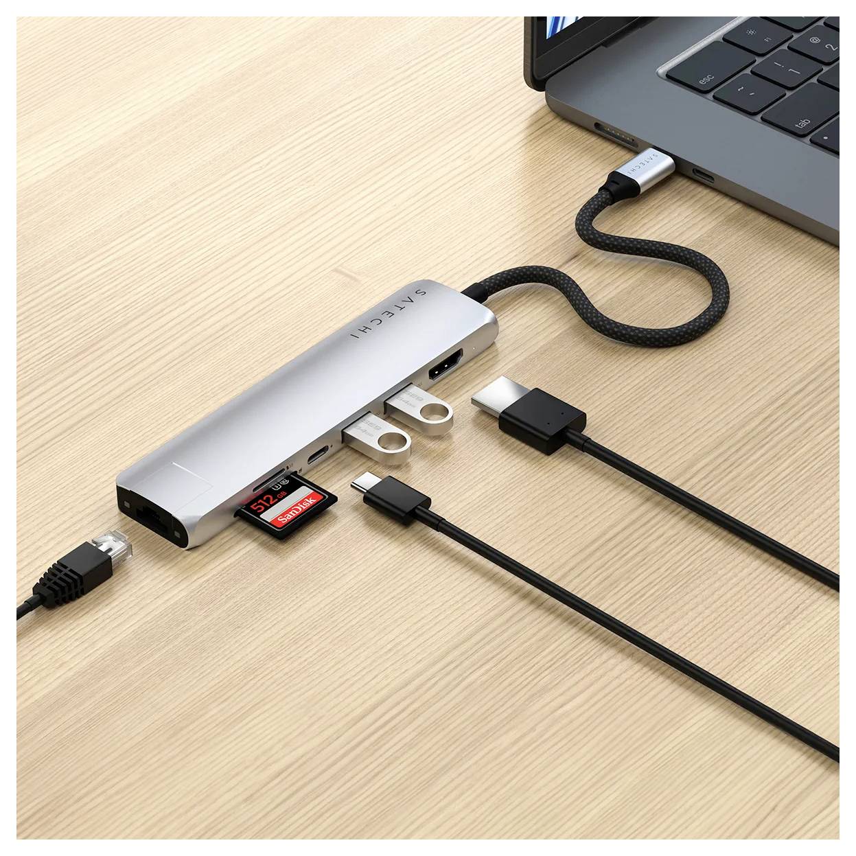 Un ordinateur portable est connecté à un hub USB-C qui offre plusieurs ports, notamment HDMI, USB et lecteur de cartes. Sur une table en bois.