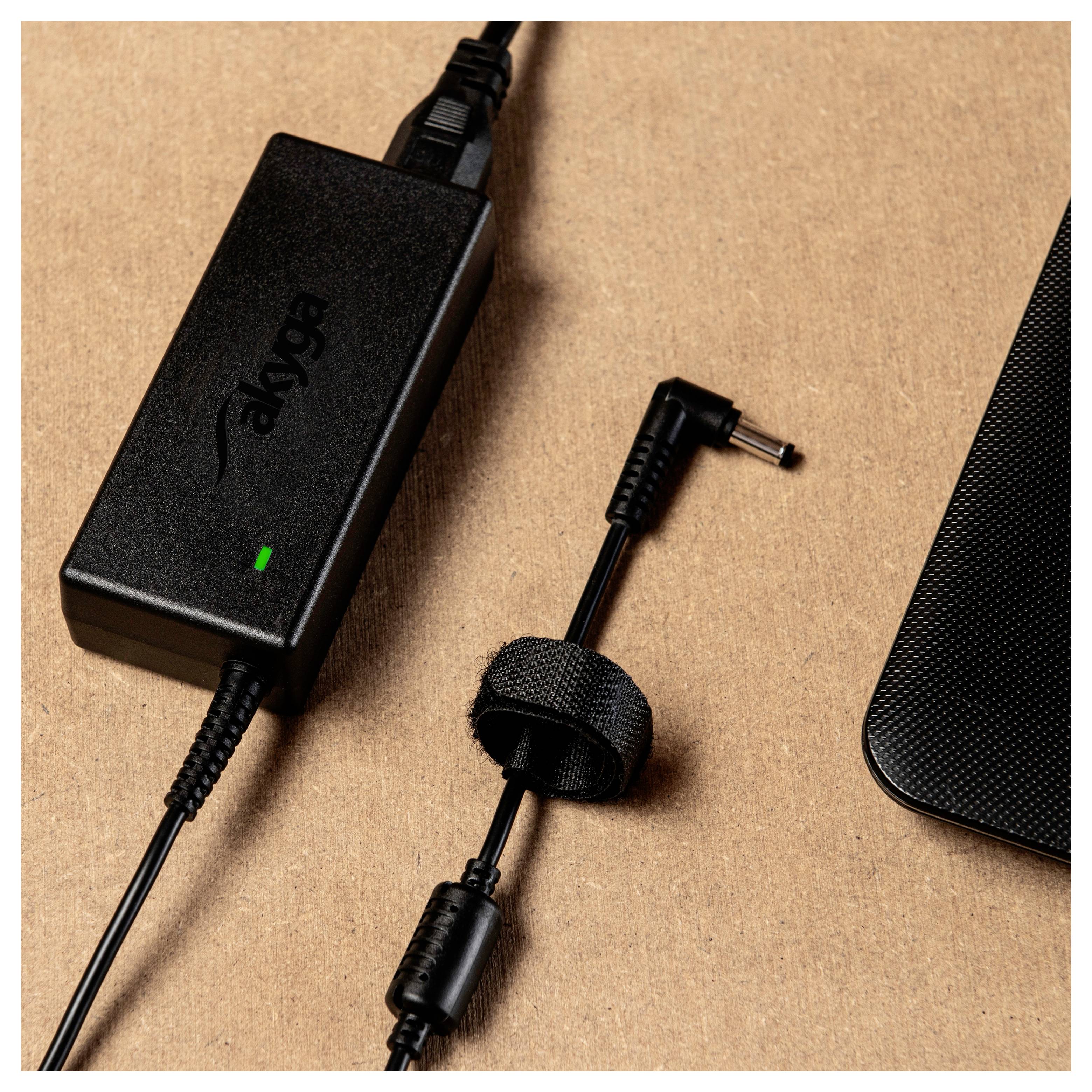 Un bloc d'alimentation noir avec un câble et une fiche repose sur une surface brune. Une sangle maintient le câble assemblé.
