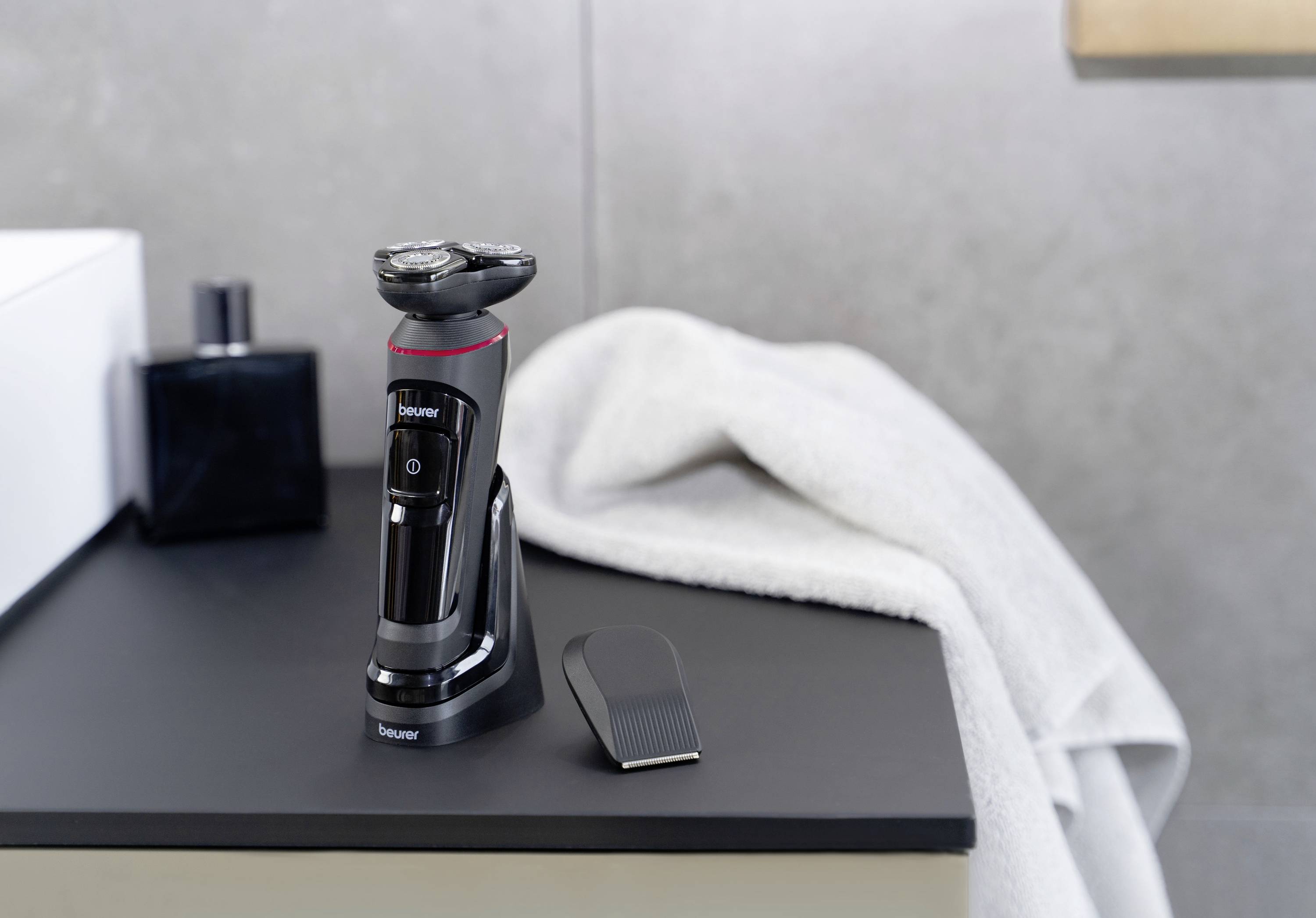 Rasoir électrique sur une étagère de salle de bain à côté d'une serviette. Un accessoire de peigne est posé à côté. L'arrière-plan est moderne et minimaliste.