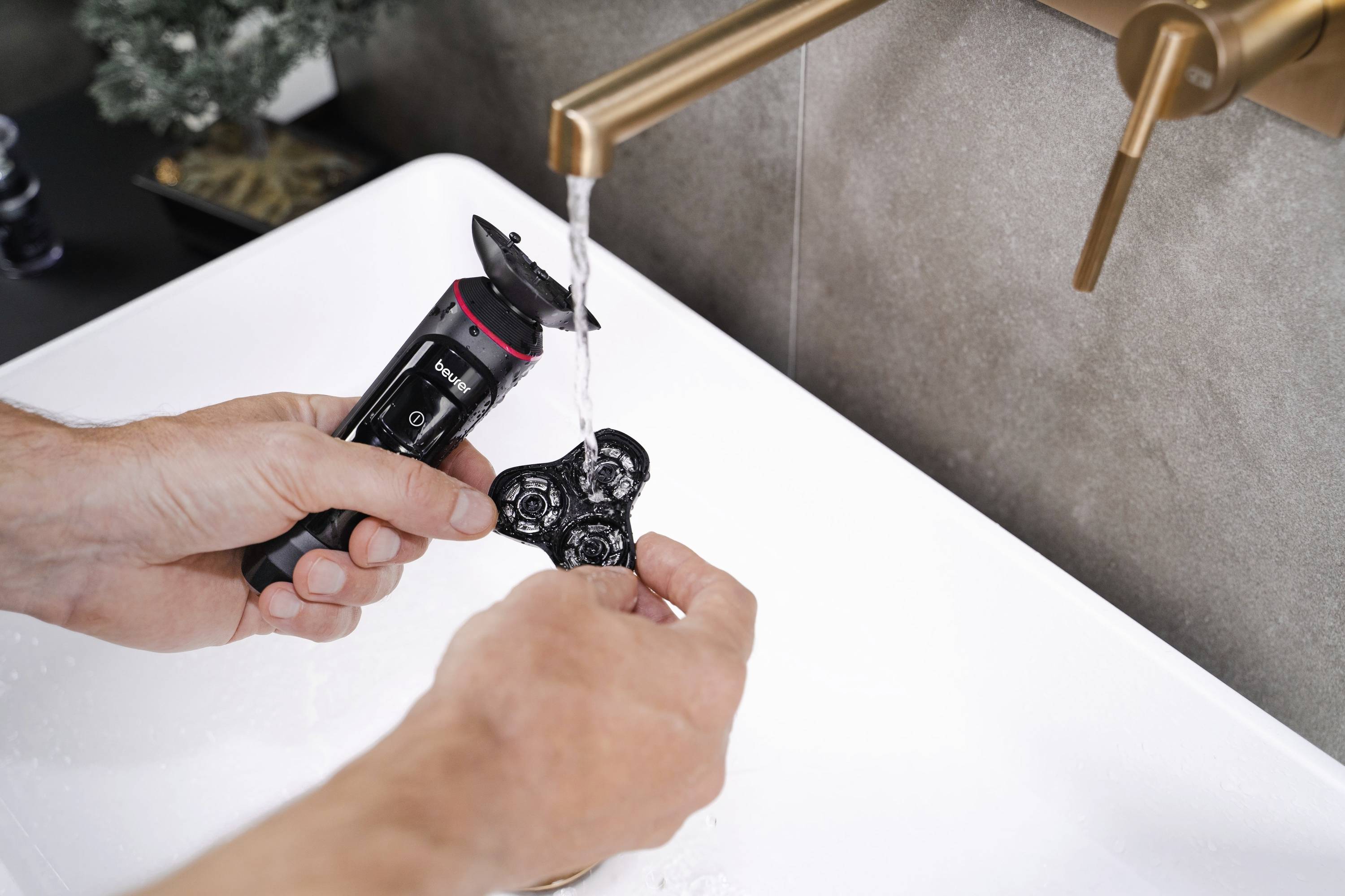 Une personne nettoie la tête de rasoir amovible d'un rasoir électrique sous l'eau courante dans l'évier.