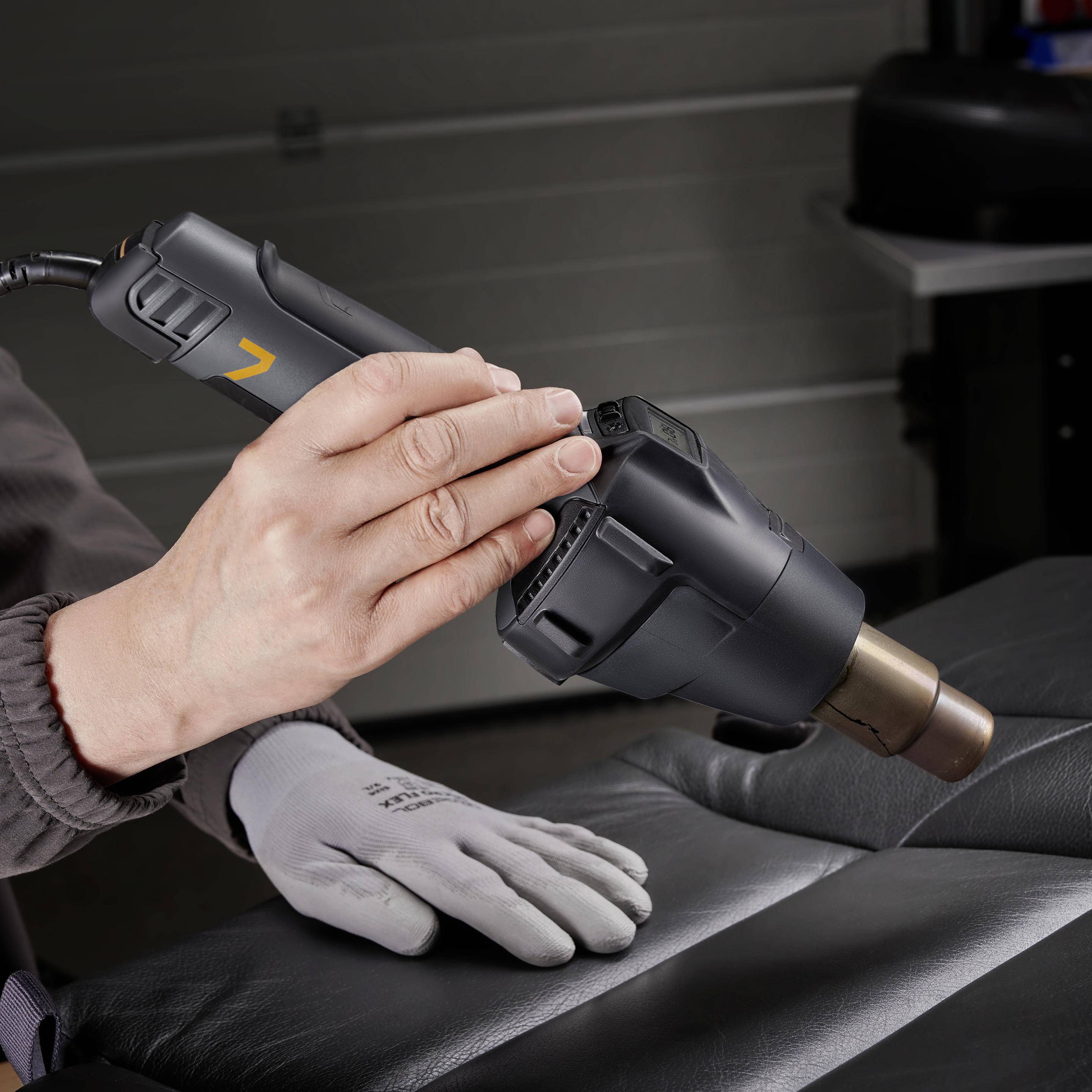 Une personne tient un pistolet à air chaud noir, probablement en travaillant sur des meubles rembourrés dans un environnement d'atelier.