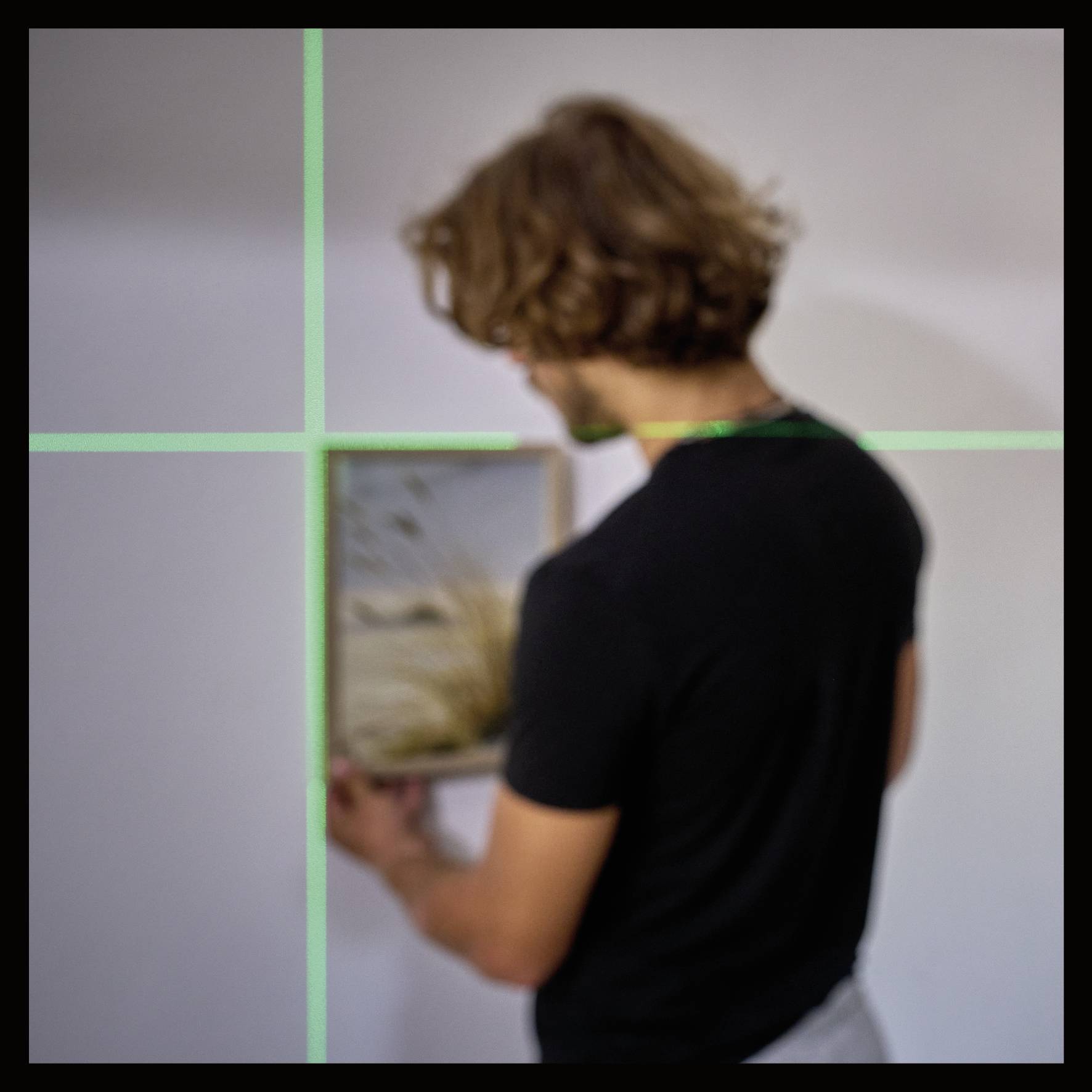 Une personne aux cheveux bruns tient un cadre photo dans une pièce aux murs blancs, avec des lignes vertes projetées sur l'image.