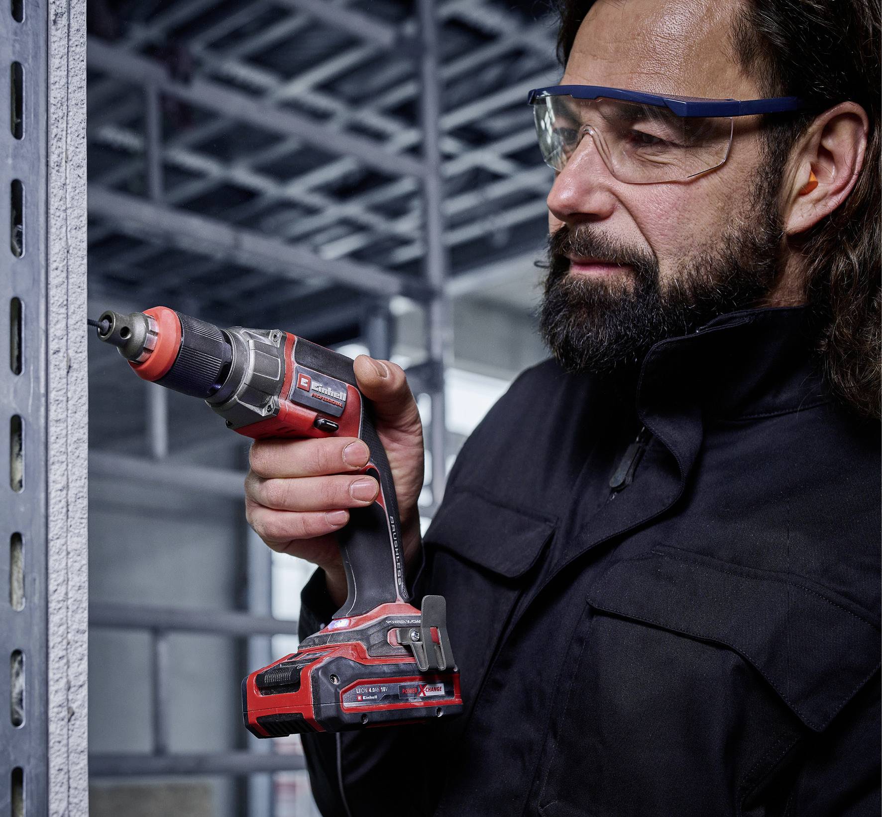 Une personne utilise une perceuse électrique pour percer des trous dans une étagère en rails métalliques. Elle porte des lunettes de protection.