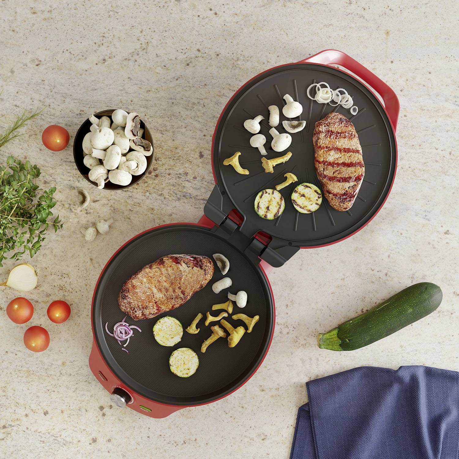 Deux grils électriques ouverts avec de la viande et des légumes grillés. À côté, des ingrédients frais comme des champignons, des tomates et des courgettes sont disposés sur une table.