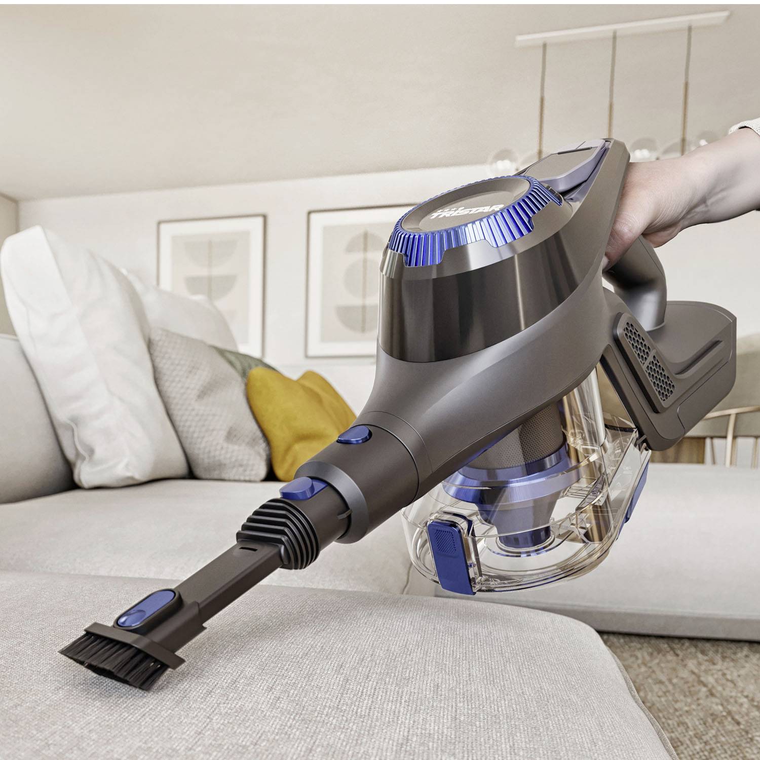 Une personne utilise un aspirateur sans fil à main pour enlever la poussière d'un canapé clair. Des coussins sont visibles en arrière-plan.