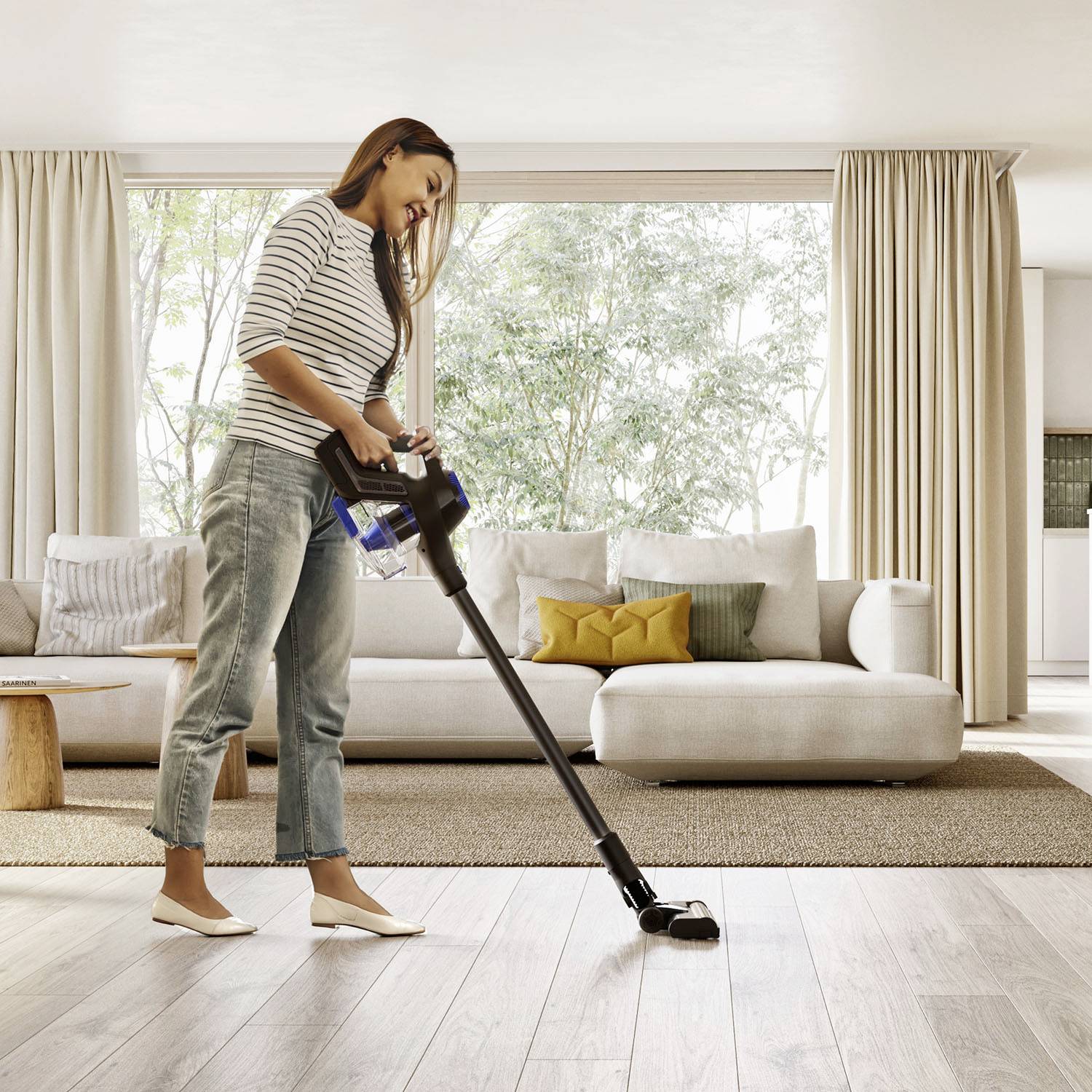 Une femme utilise un aspirateur dans un salon moderne avec des canapés et des coussins clairs. La lumière entre par de grandes fenêtres.