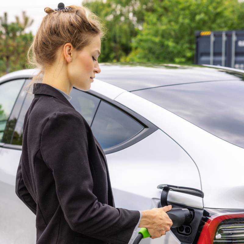 Une femme charge un véhicule électrique à l'extérieur sur une borne de recharge.