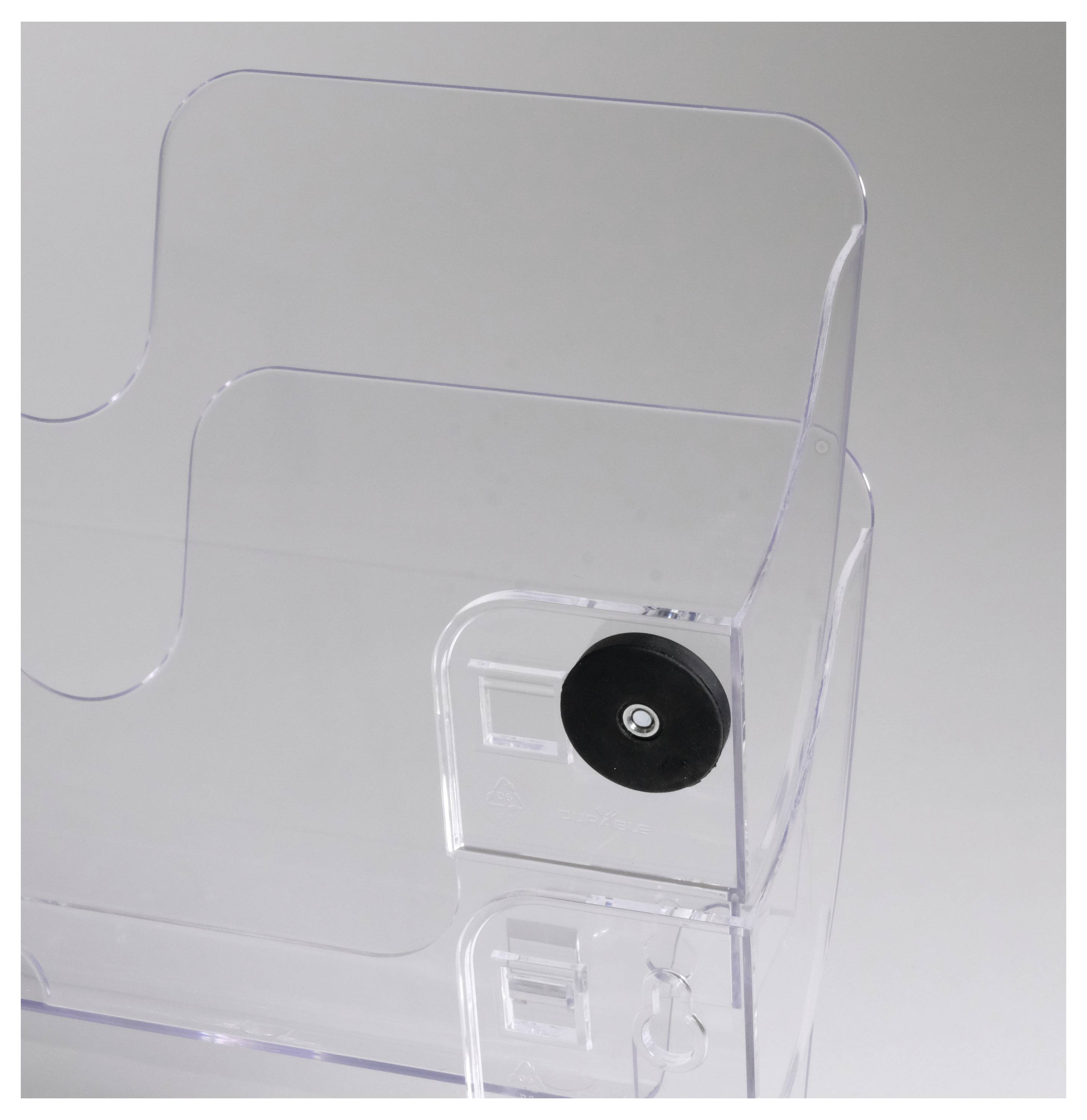 Porte-revues en plastique transparent, partiellement visible, avec un disque en caoutchouc noir sur le côté. Design épuré et minimaliste.