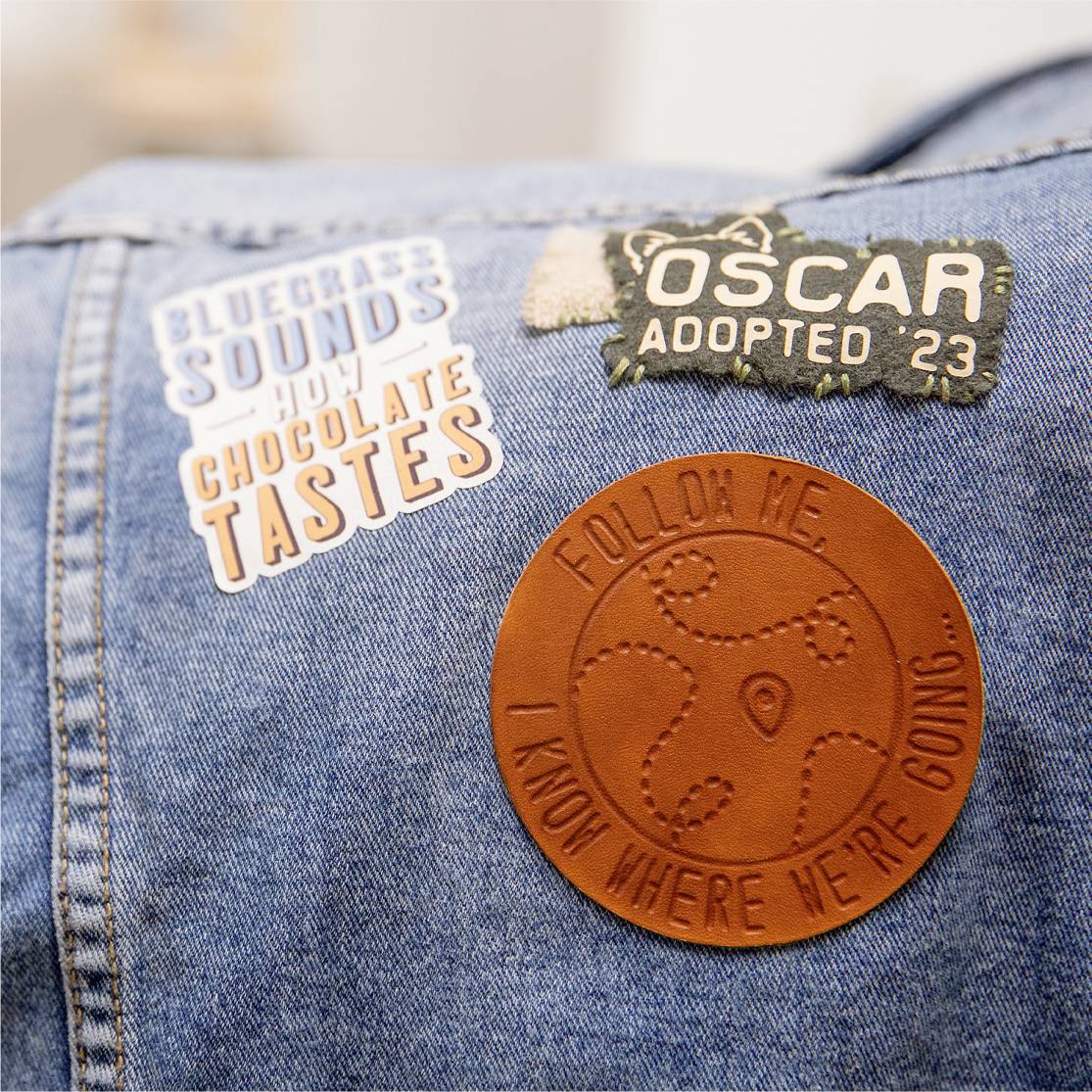 Veste en jean avec trois badges : « Sons bluegrass, goût de chocolat chaud », « Oscar Adopté '23 », et un patch en cuir « Suis-moi. Je sais où nous allons ».