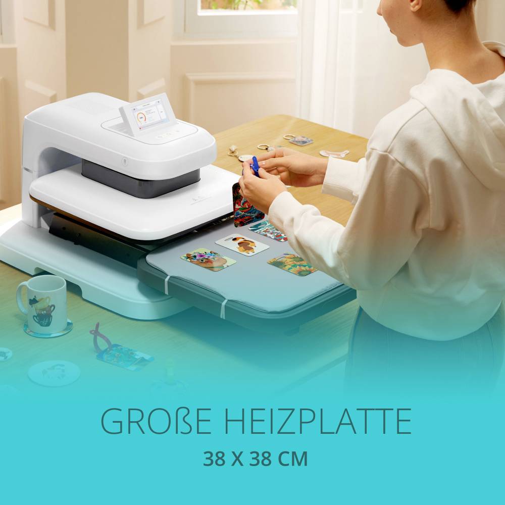 Une personne utilise un appareil de finition textile avec une grande plaque chauffante (38 x 38 cm) sur des t-shirts. Une tasse est posée à côté sur la table.
