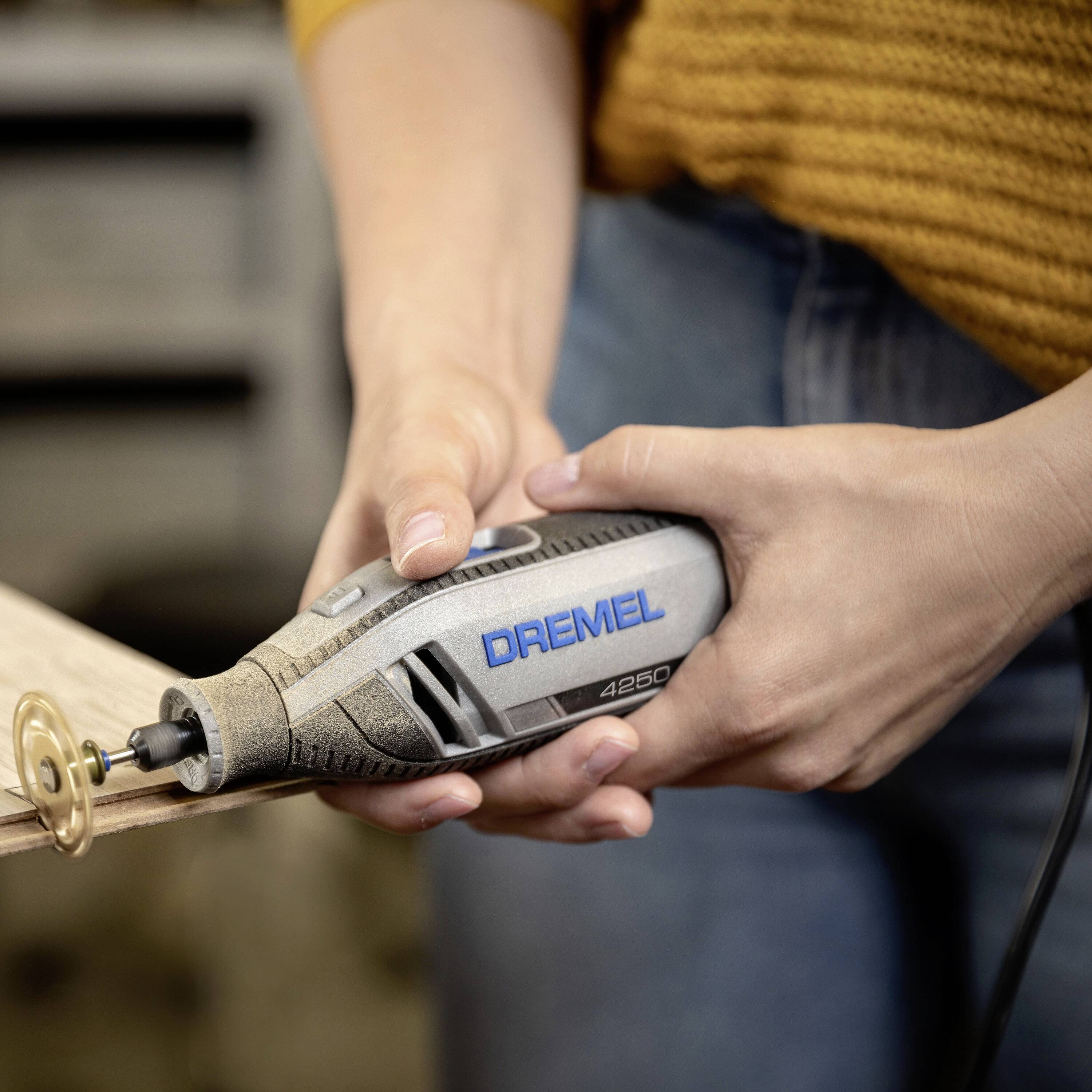 Une personne travaille le bois avec un outil Dremel. L'outil est équipé d'un embout de ponçage et est tenu à deux mains.