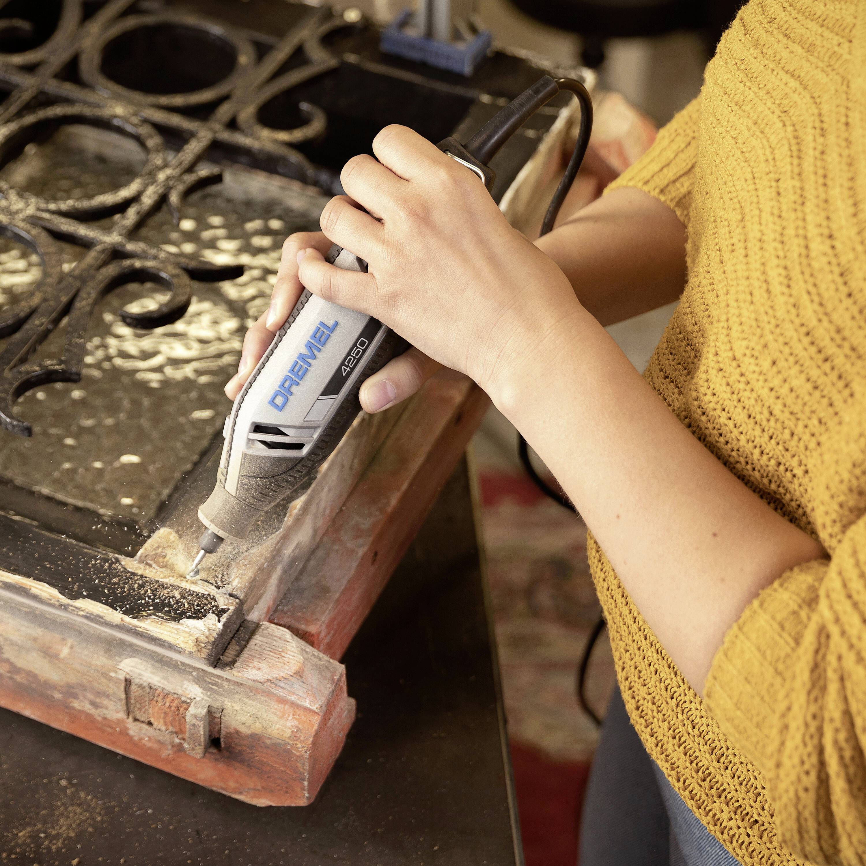 Une personne travaille avec un outil Dremel sur un cadre en bois pour sculpter des détails.
