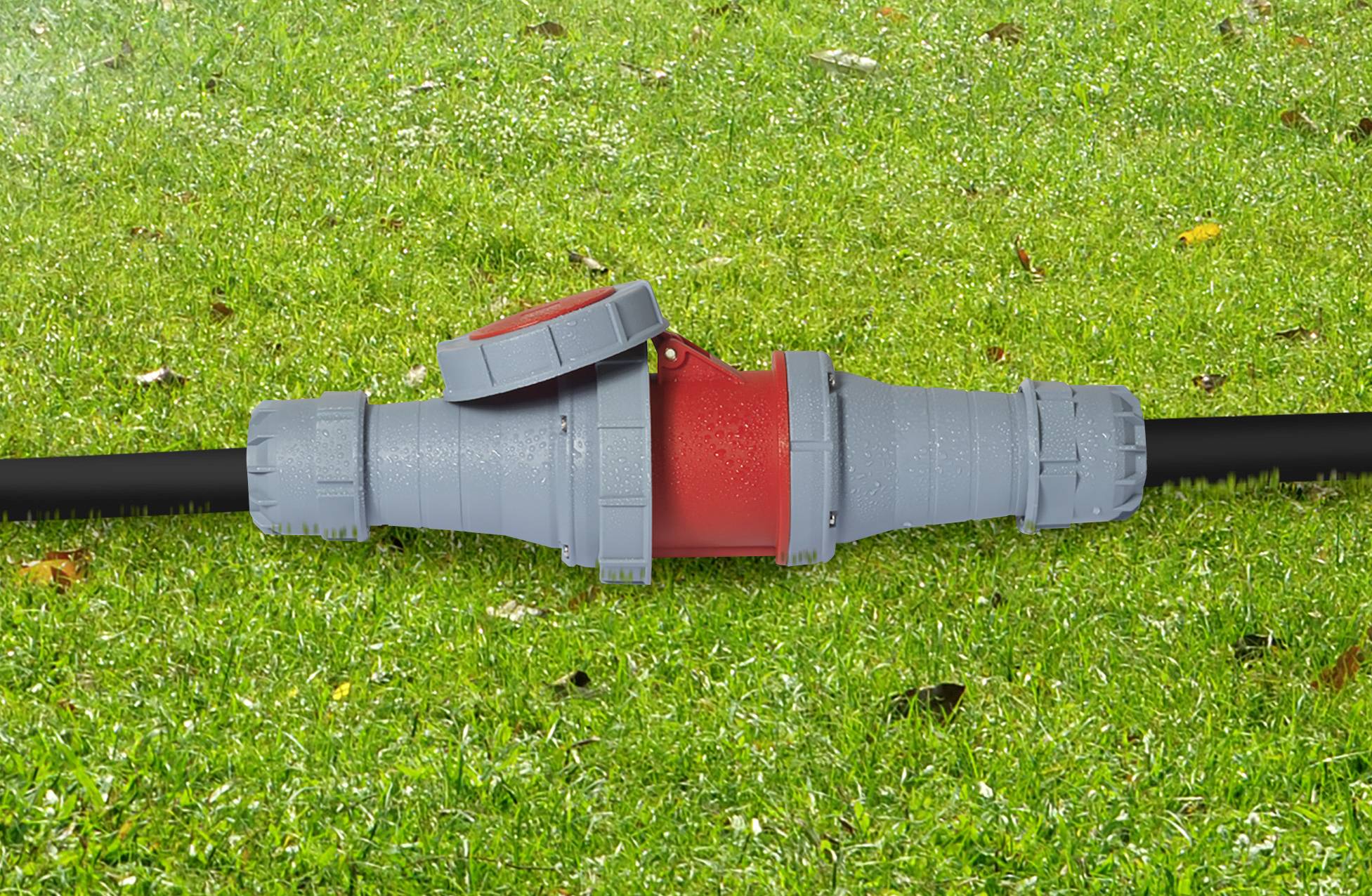 Un tuyau gris avec une partie centrale rouge et un couvercle ouvert repose sur une pelouse verte.
