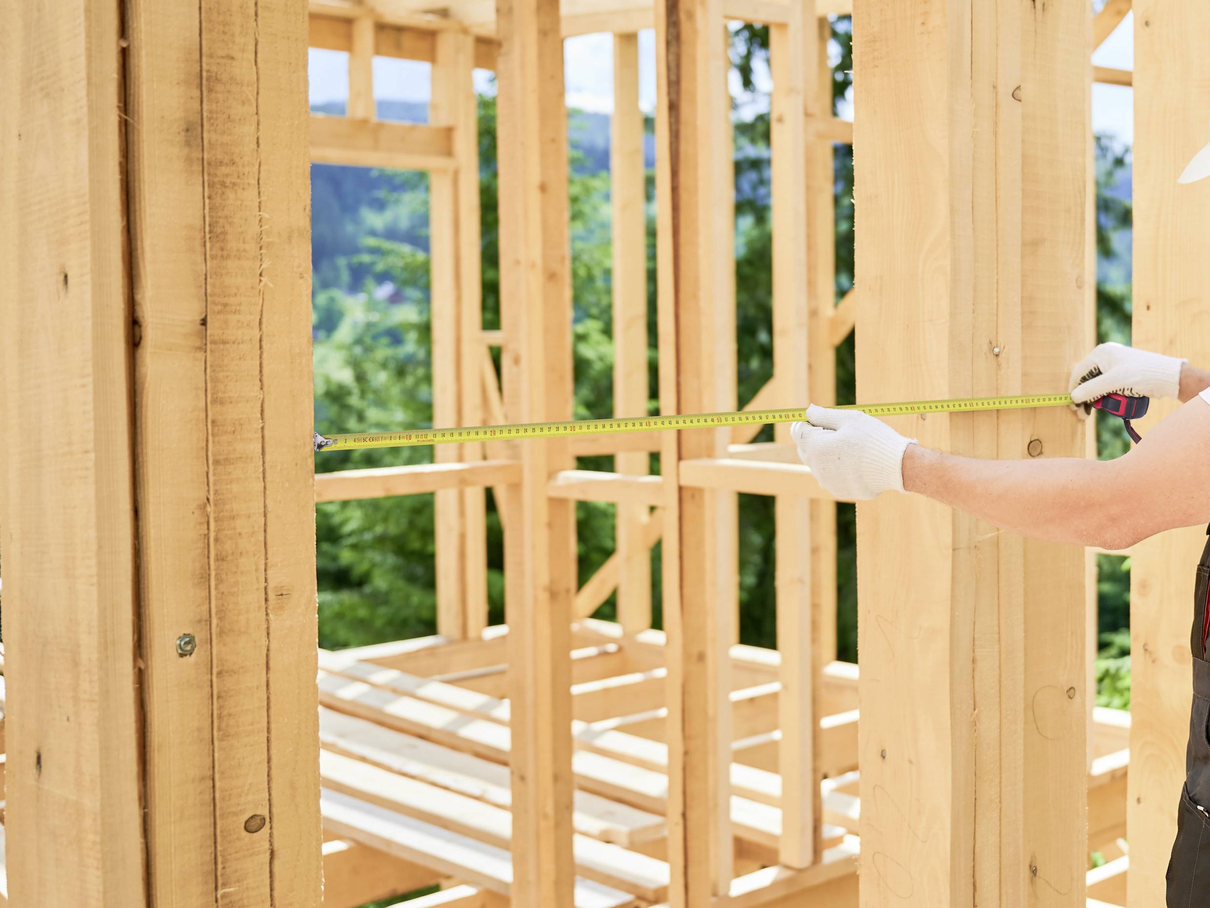 Une personne mesurant une structure en bois à l'aide d'un mètre ruban, à l'extérieur.