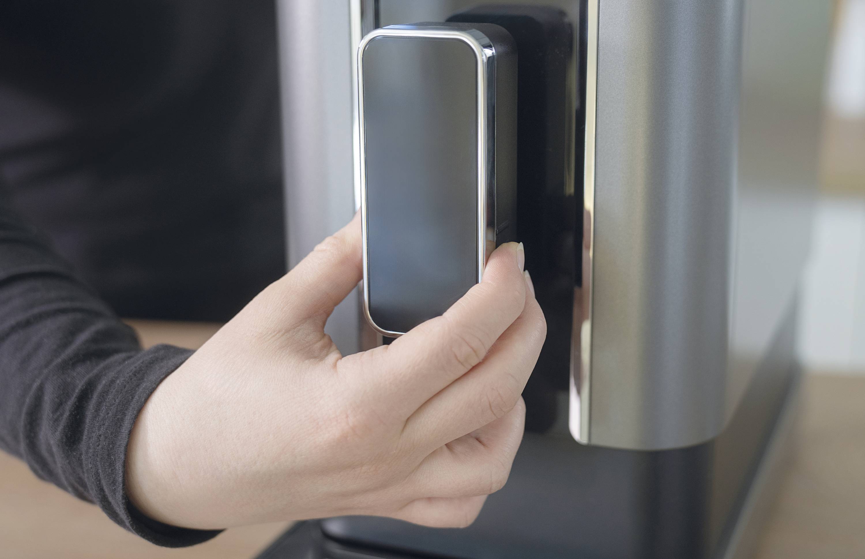 Une personne tient un smartphone contre un lecteur de carte sans contact, probablement pour effectuer un paiement.