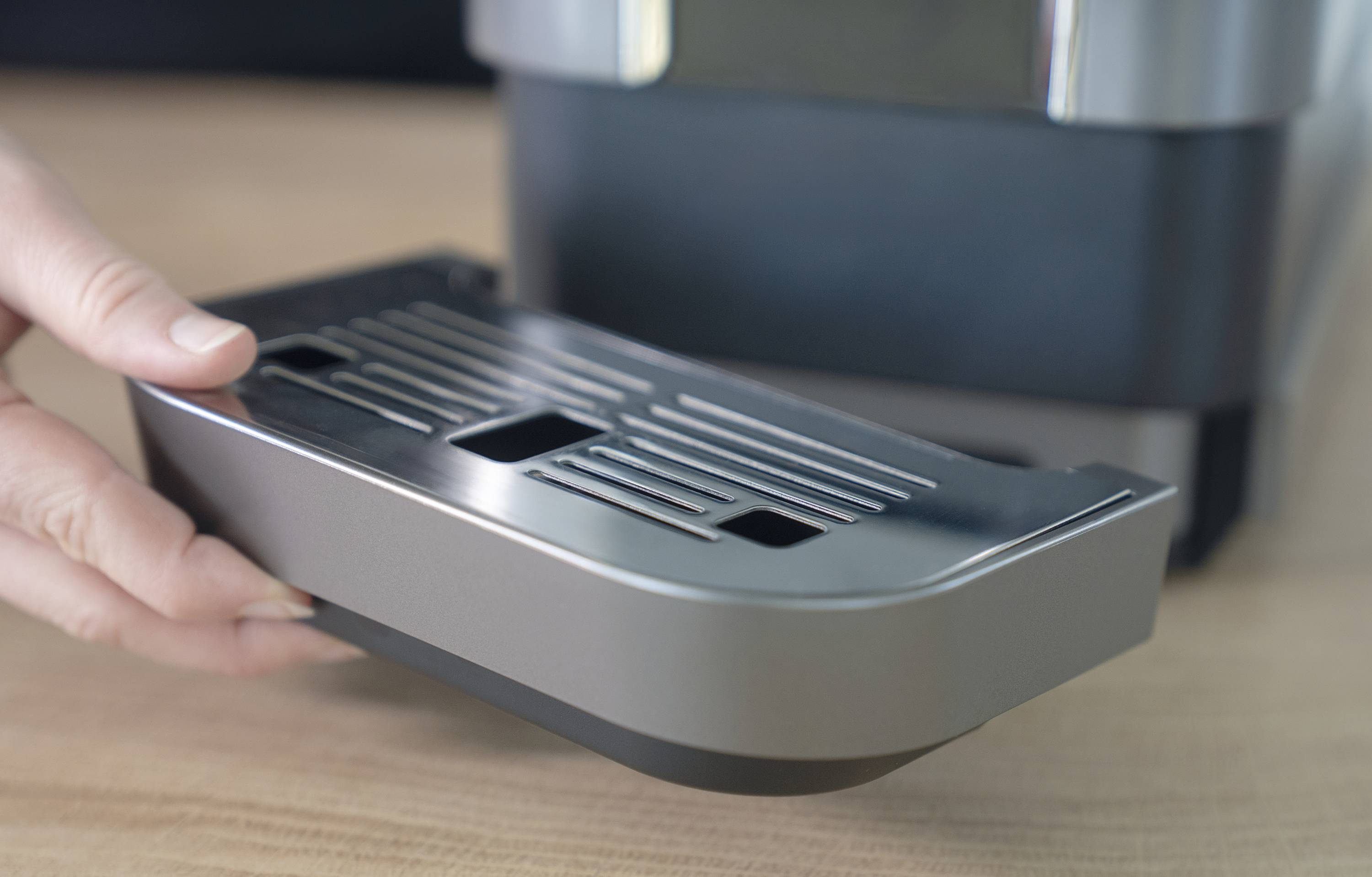 Une main retire le bac d'égouttement d'une machine à café posée sur un support en bois.