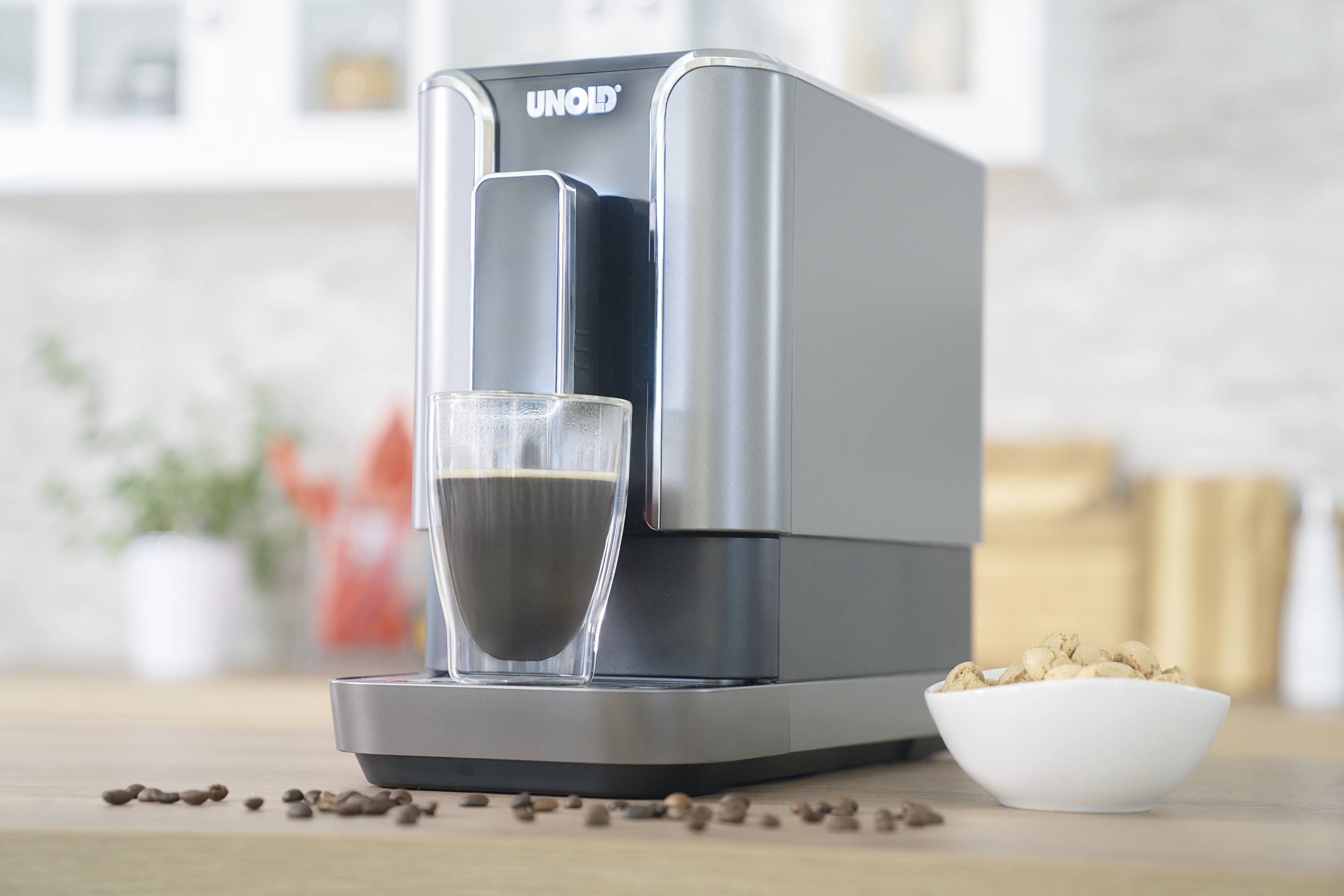 Une machine à café sur une table de cuisine prépare du café noir dans un verre. À côté se trouve un bol de noix.