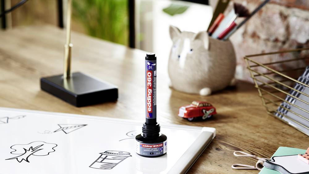 Un tableau blanc sur un bureau où des croquis sont visibles. À côté se trouvent un marqueur Edding 360 et un porte-stylos en forme de chat.
