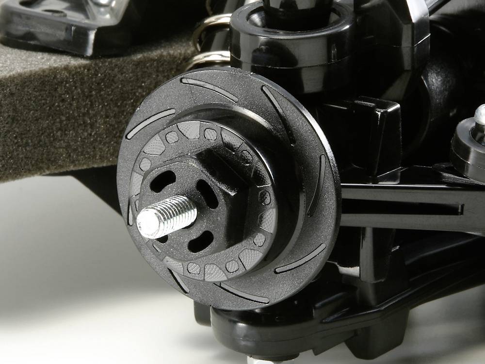 Gros plan sur un système de roue de voiture télécommandée noir, avec disque de frein et suspension de roue. Mécanisme détaillé visible.