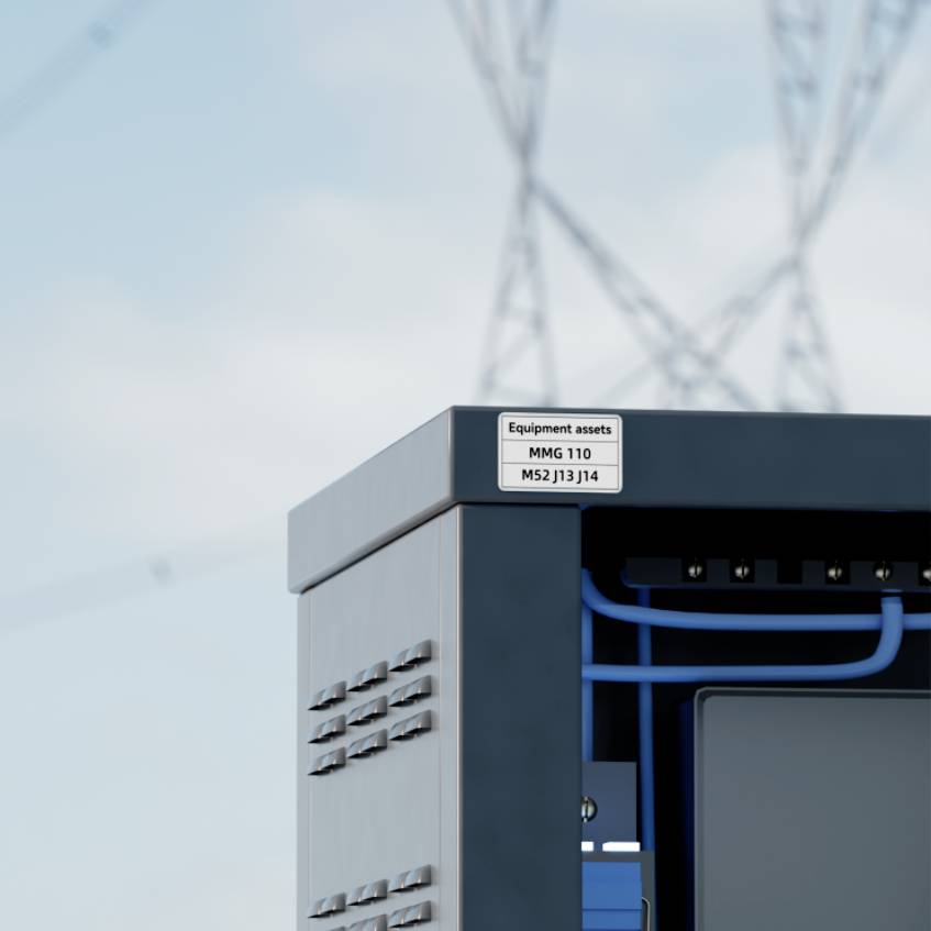 Boîtier électrique à l'extérieur sous un poteau électrique, avec une étiquette visible indiquant « Equipment assets MMG 110 M52 J13 J14 ».