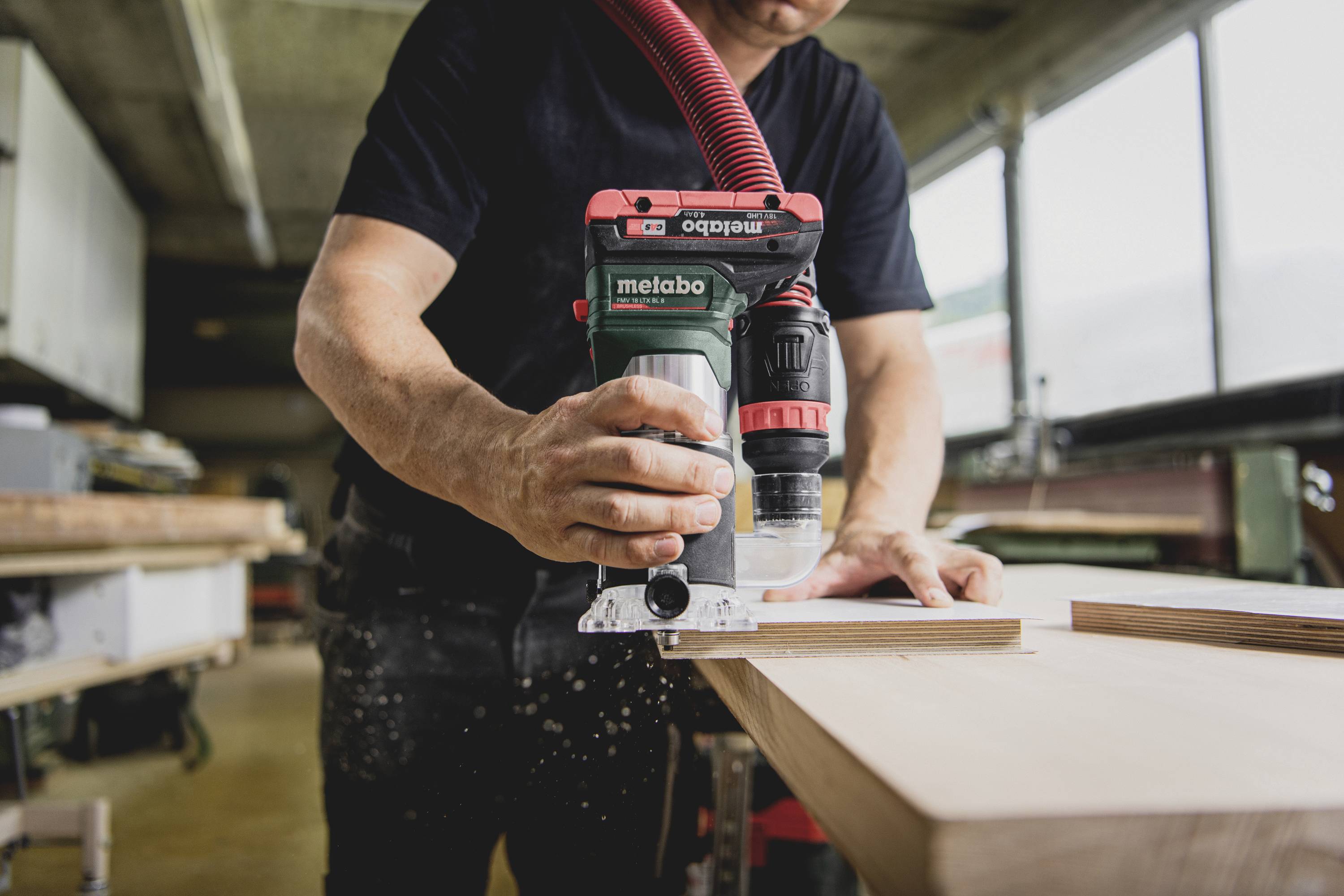 Un artisan travaille une planche de bois avec un outil électrique dans un atelier. L'outil porte l'inscription « metabo ».