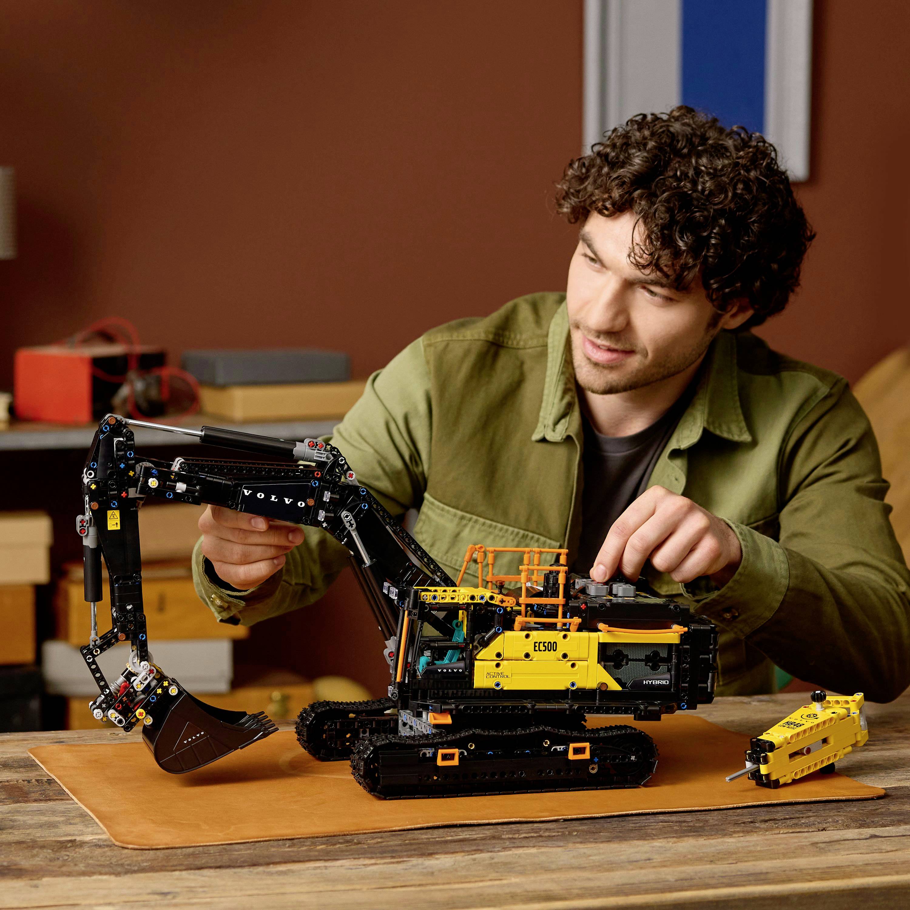 Une personne assemble un modèle détaillé d'excavatrice LEGO sur une table, montrant une construction complexe et des détails réalistes avec des composants jaunes et noirs.