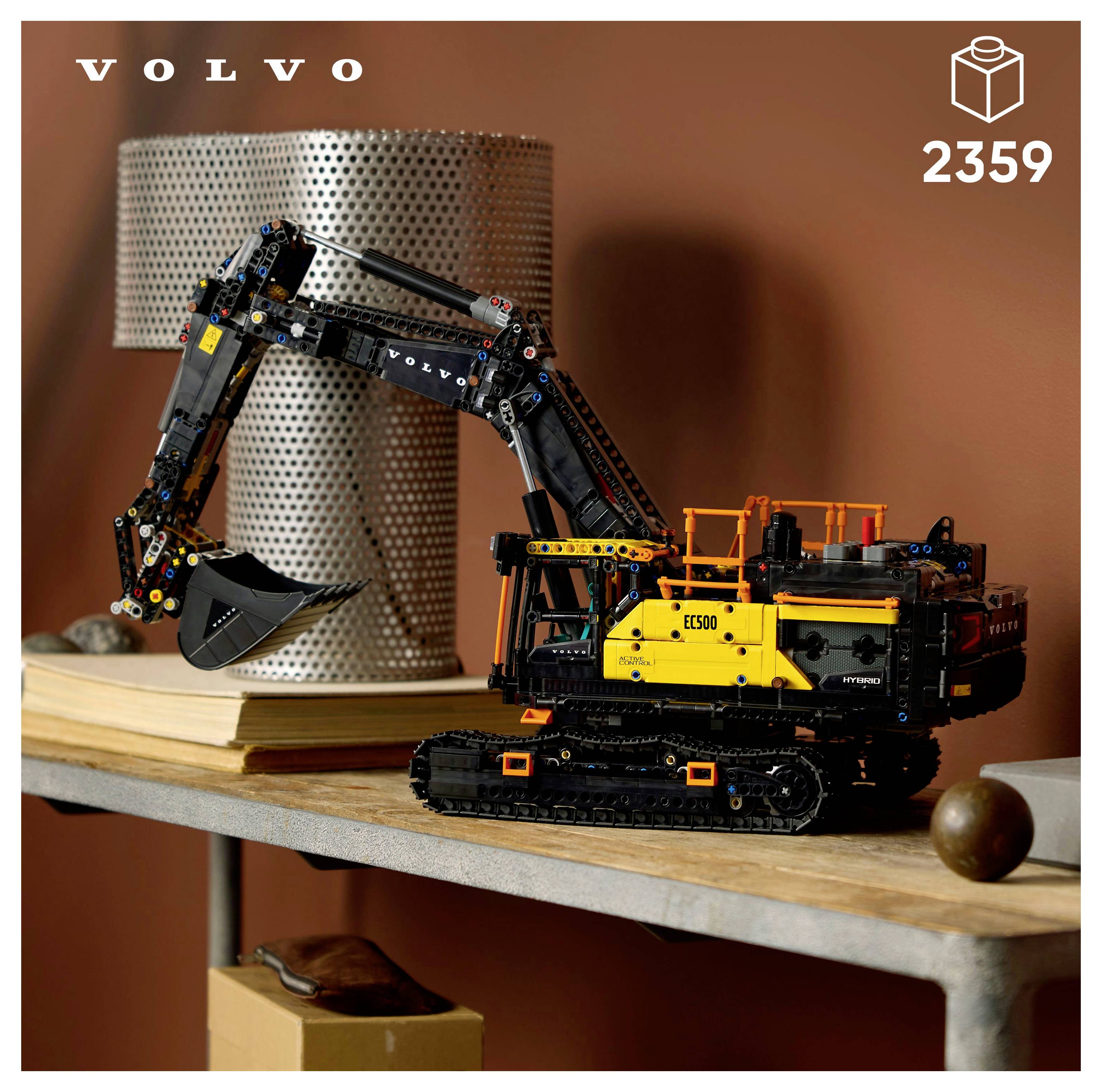 Modèle d'une pelle excavatrice Volvo, construite avec des pièces LEGO, exposé sur une table avec un conteneur cylindrique en métal et quelques éléments décoratifs à proximité.