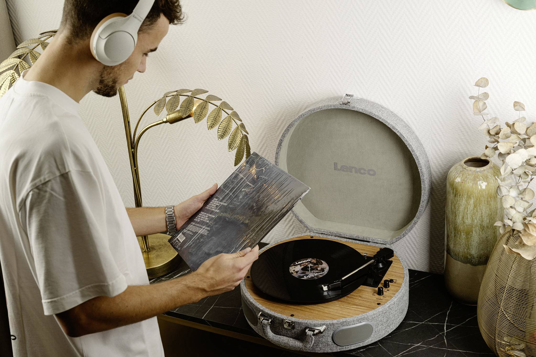 Un homme portant des écouteurs examine un album vinyle à côté d'une platine tourne-disque dans une pièce au design moderne.
