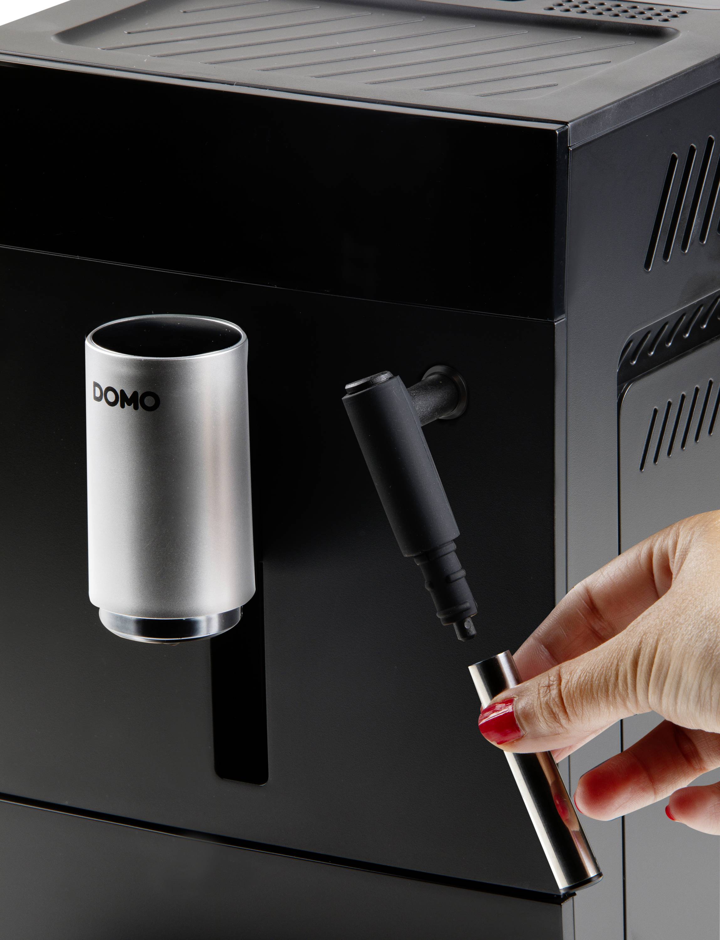 Une machine à café noire avec un gobelet argenté. Une main tient un stylo métallique près de l'appareil.