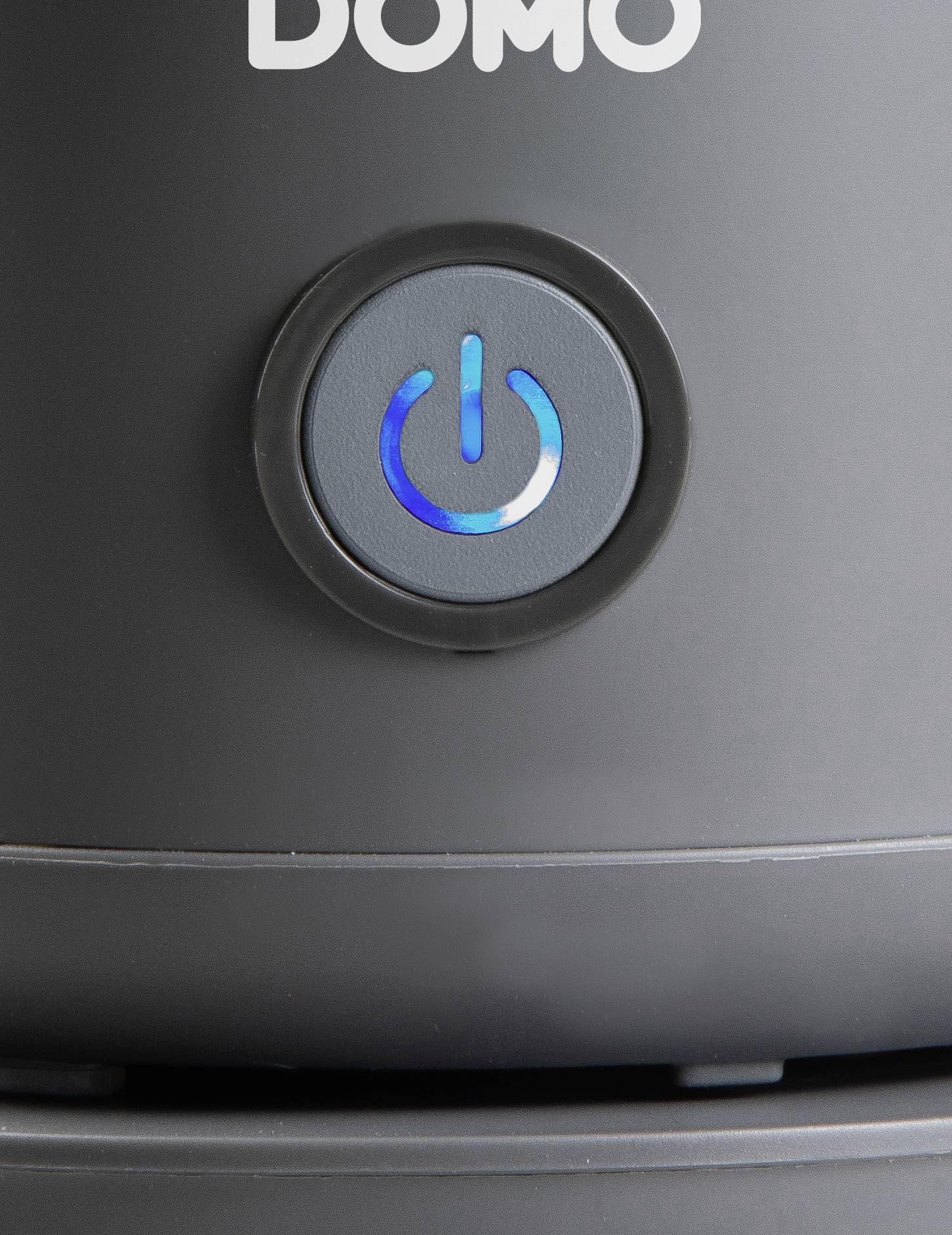 Un bouton électronique noir avec un symbole lumineux bleu de marche/arrêt sur un appareil. Au-dessus est inscrit 'Domo'.
