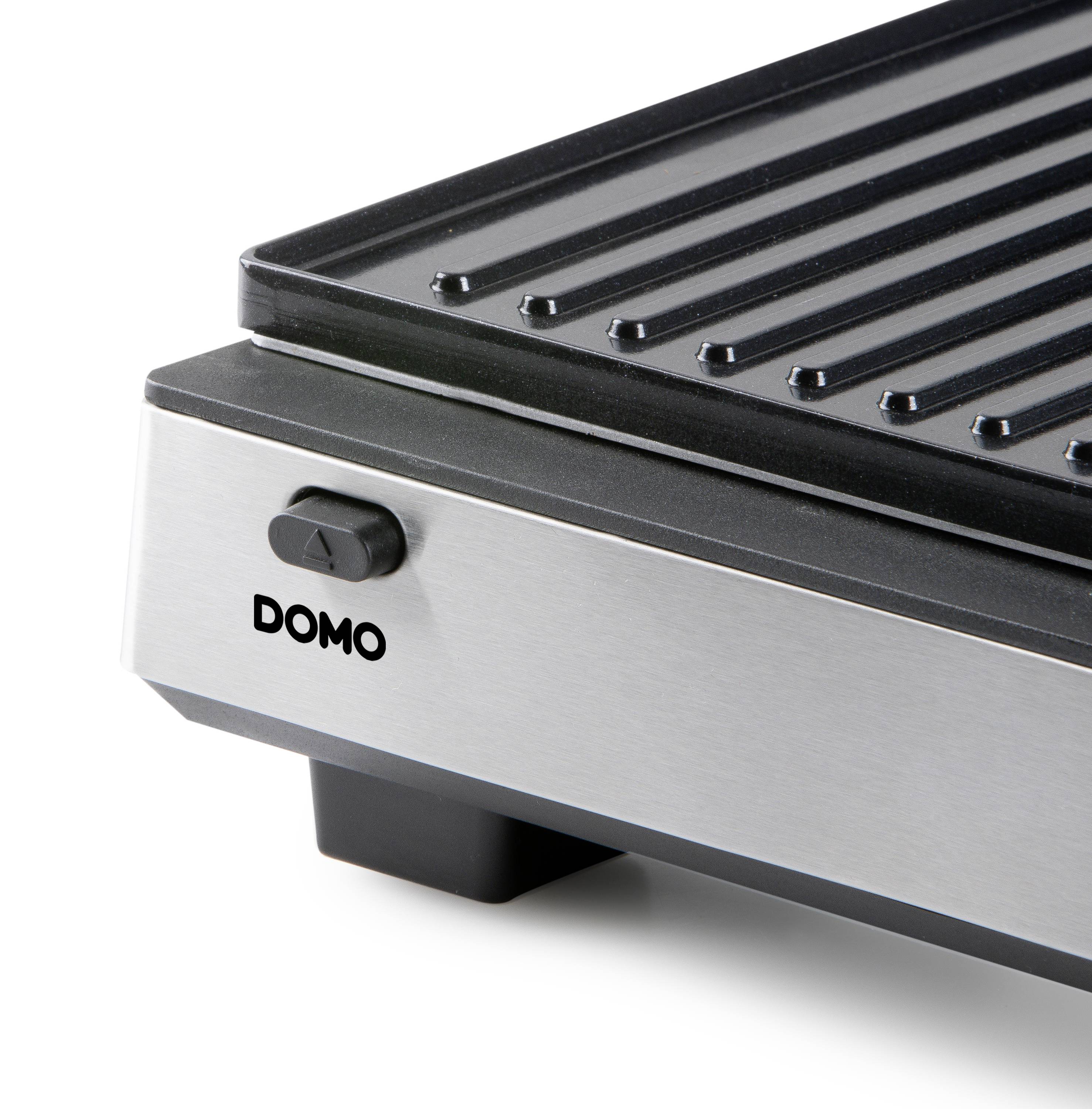 Un grill argenté et noir avec une surface striée et un interrupteur sur le côté. Sur le devant, il est inscrit 'DOMO'.