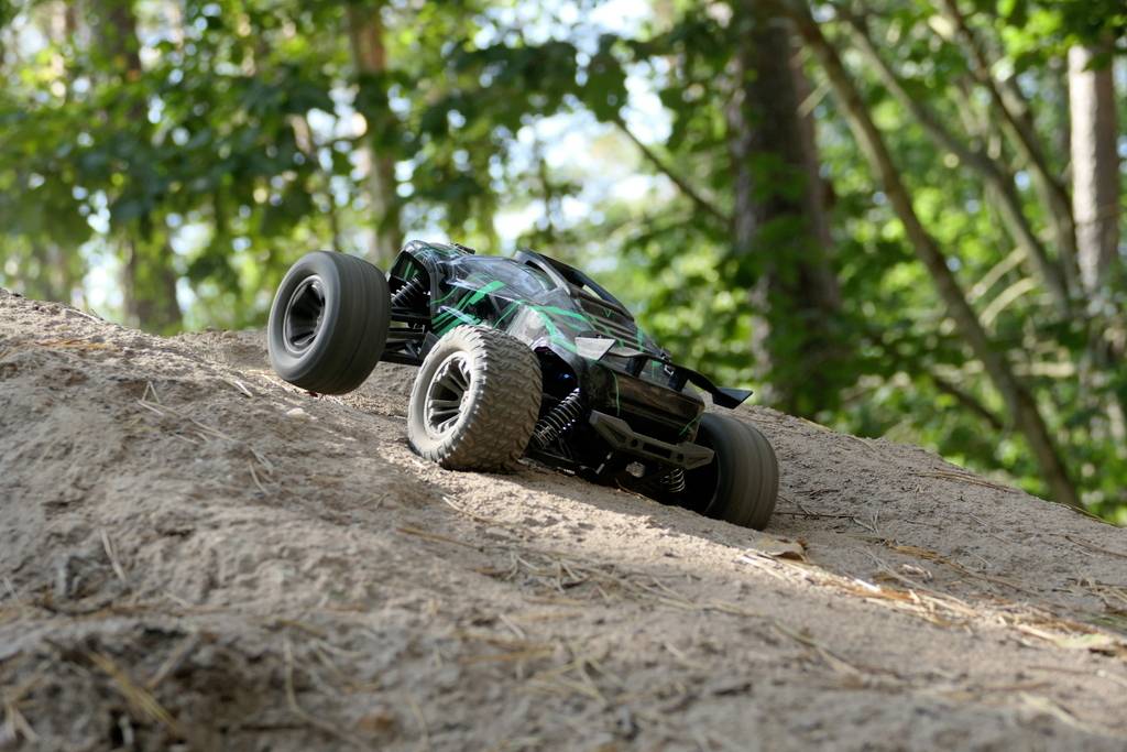 Une voiture télécommandée monte une pente sablonneuse dans la forêt, entourée d'arbres verts.