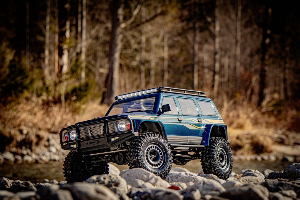 Une voiture miniature tout-terrain est posée sur des rochers devant un arrière-plan naturel flou.