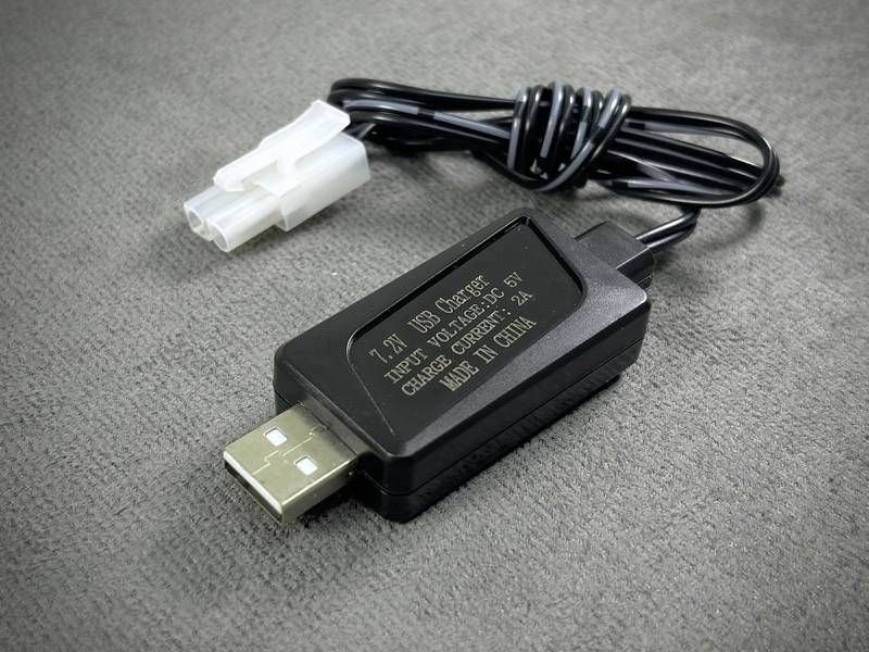 Câble de données USB avec adaptateur rectangulaire, posé sur un tapis. L'adaptateur porte une inscription indiquant la puissance de charge et le pays d'origine.