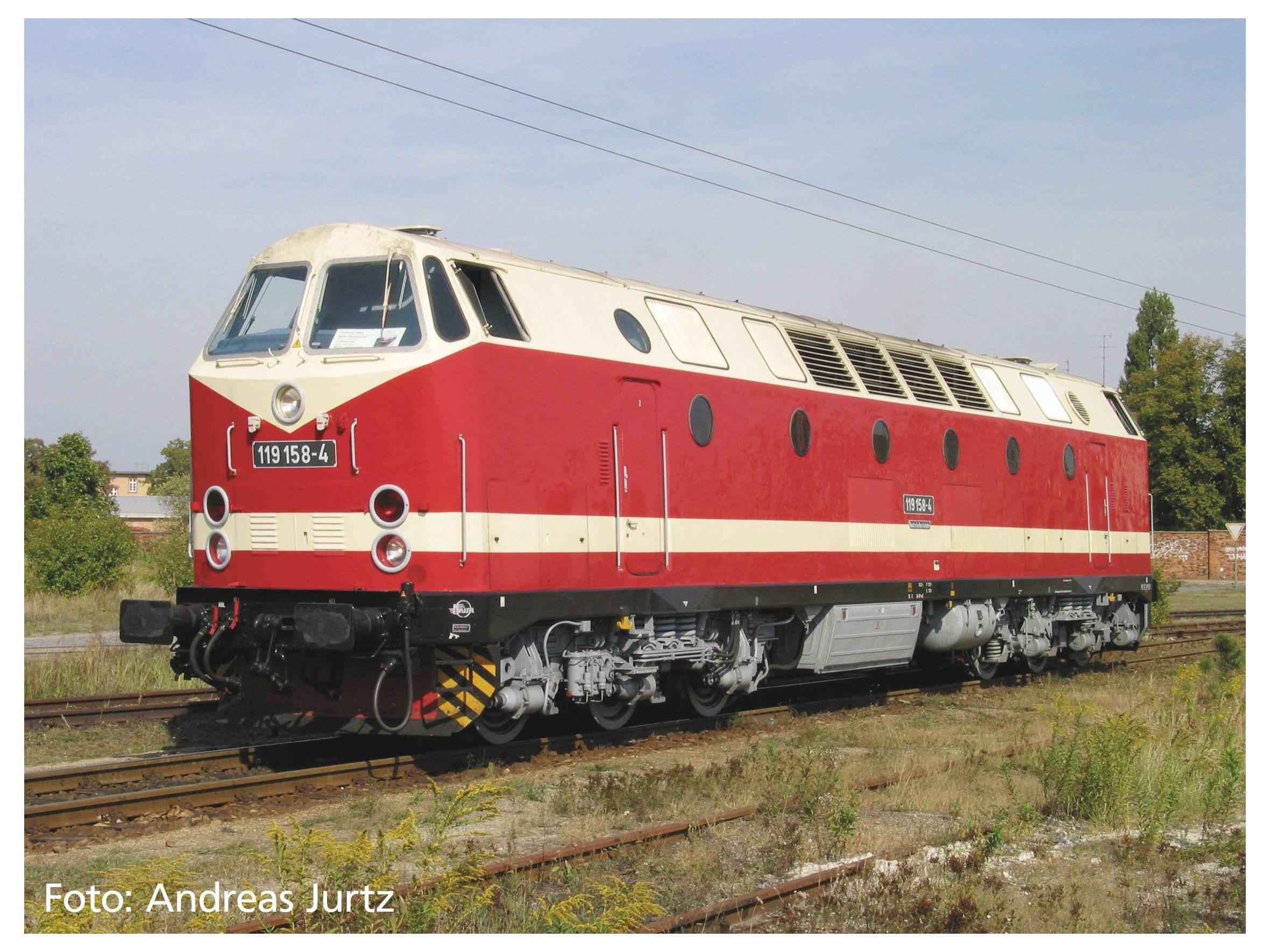 Une locomotive diesel rouge et crème sur une voie ferrée. Elle possède des fenêtres rondes et des ouvertures de ventilation sur le dessus.